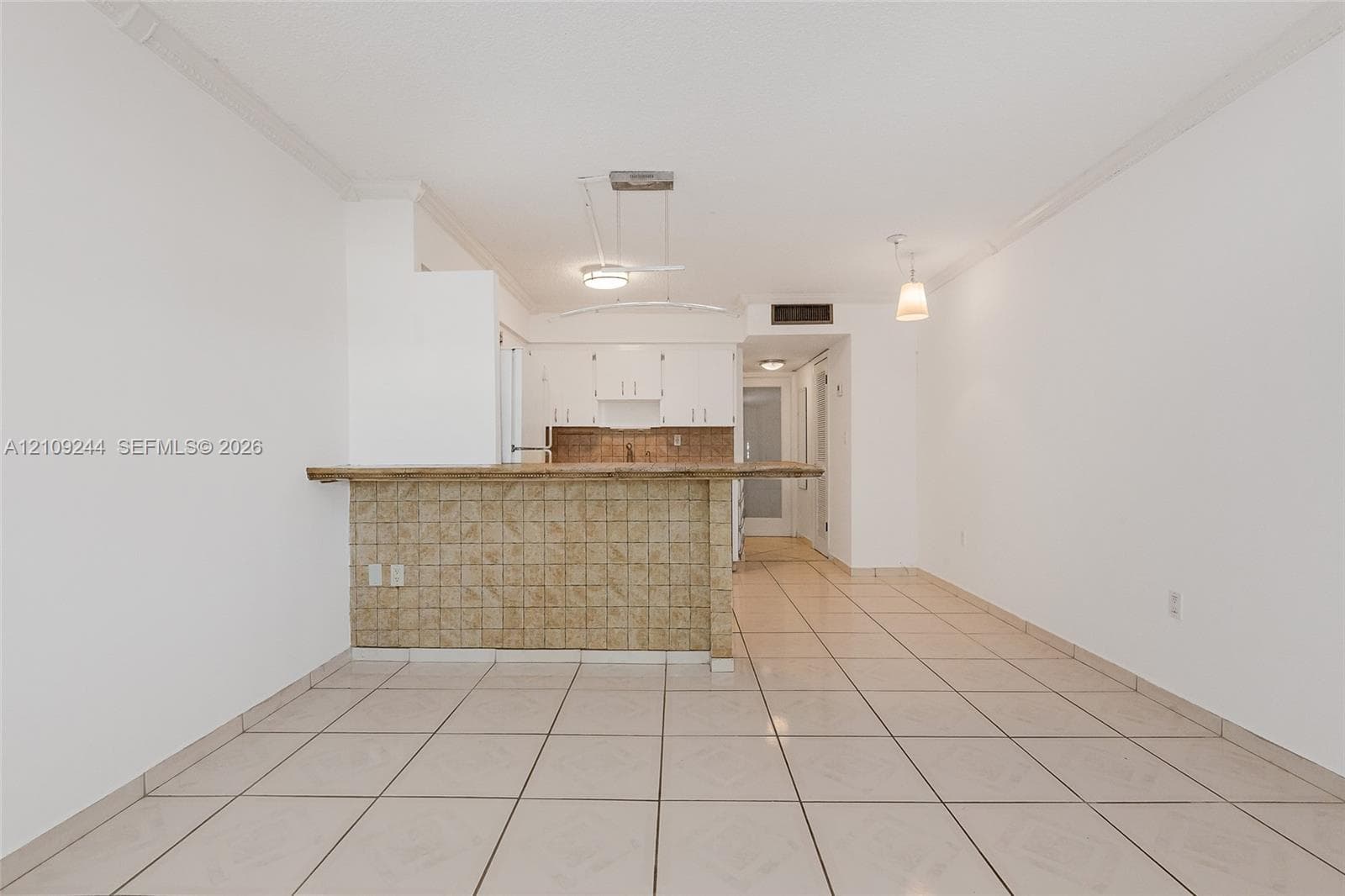 Open floor plan featuring ceramic tile flooring, a breakfast bar with decorative tile cladding, white upper cabinetry, and suspended pendant lighting