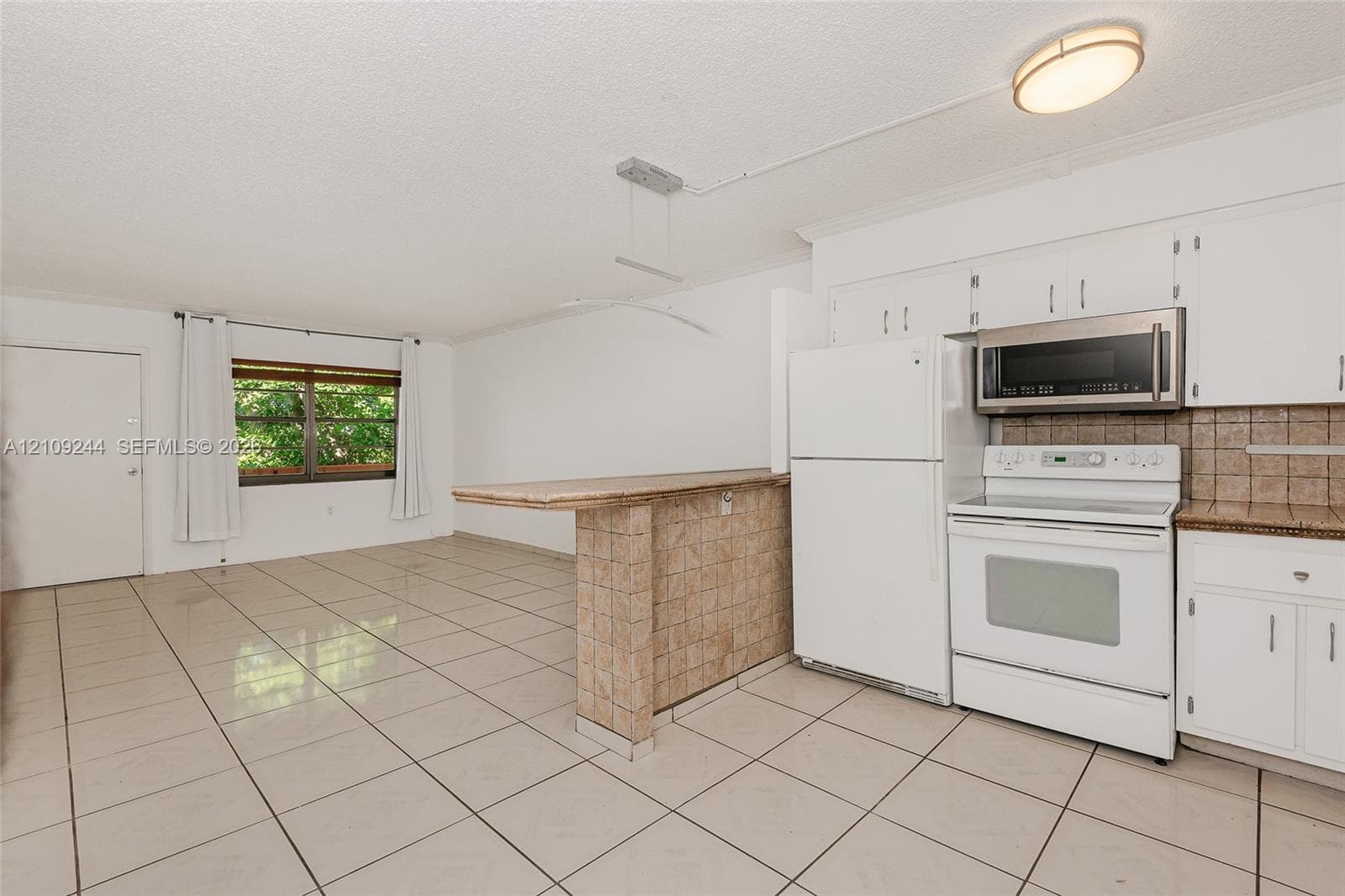 Kitchen featuring tile flooring, white cabinetry, a built-in stone-finish breakfast bar, and integrated white appliances