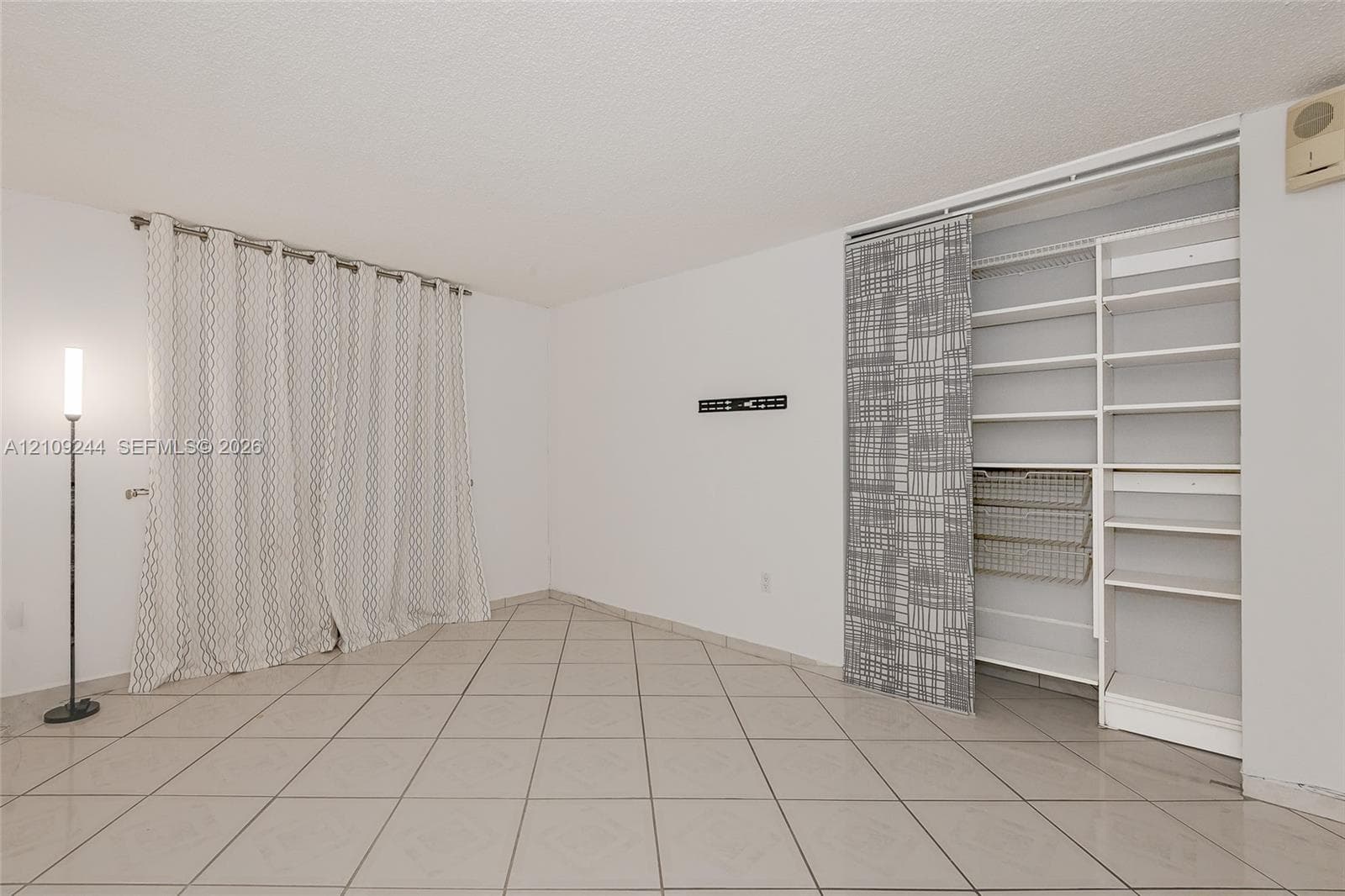 Interior space featuring neutral tile flooring, built-in wall shelving with integrated wire baskets, and sliding panel doors