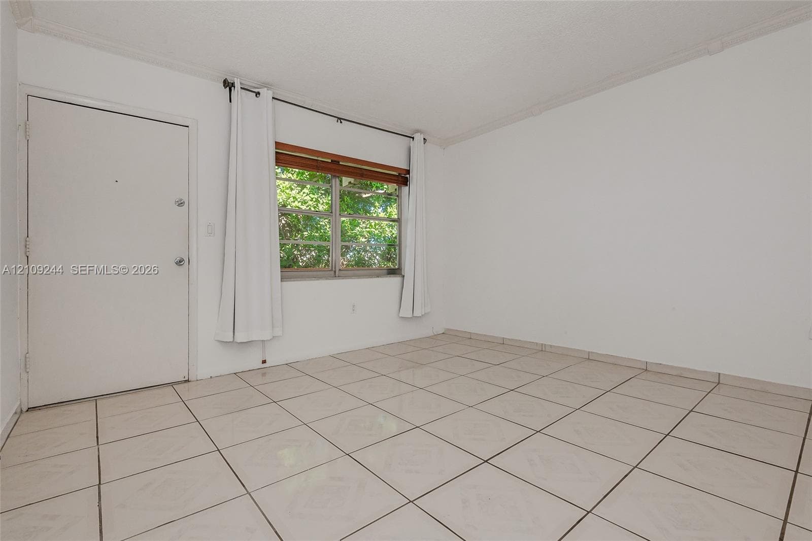 Interior room featuring neutral ceramic tile flooring, a solid core door, and a horizontal window with a wooden valance