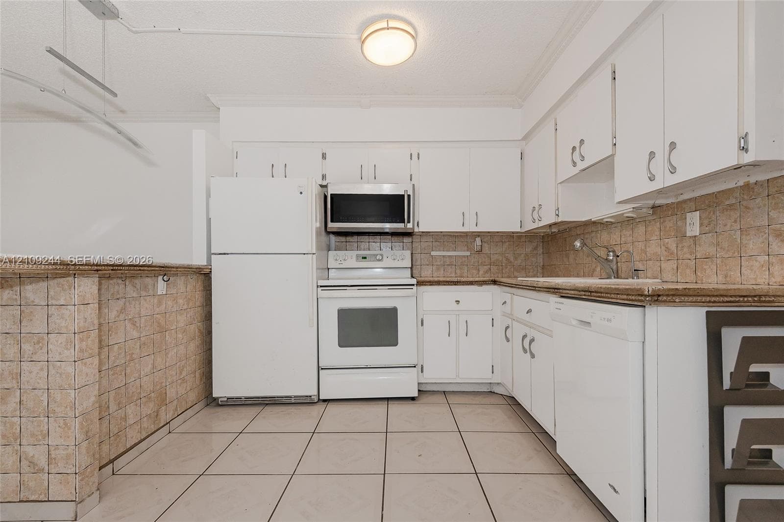 Kitchen featuring white cabinetry, tile backsplash, tile flooring, and integrated white appliances including a dishwasher, range, and microwave
