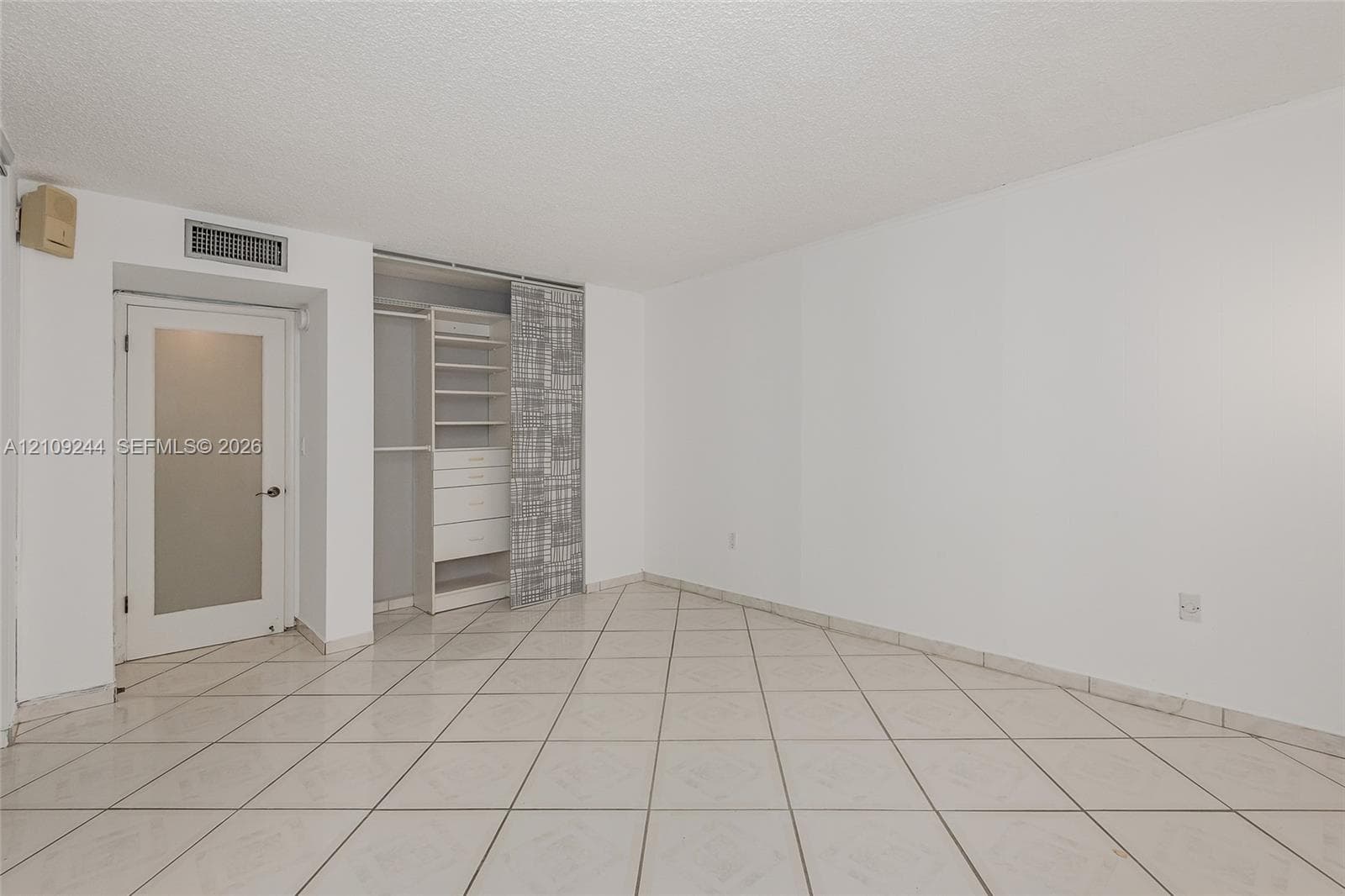 Ceramic tile flooring arranged in a diagonal pattern, interior door with a frosted glass panel, and custom built-in closet organization system featuring shelving and integrated drawers