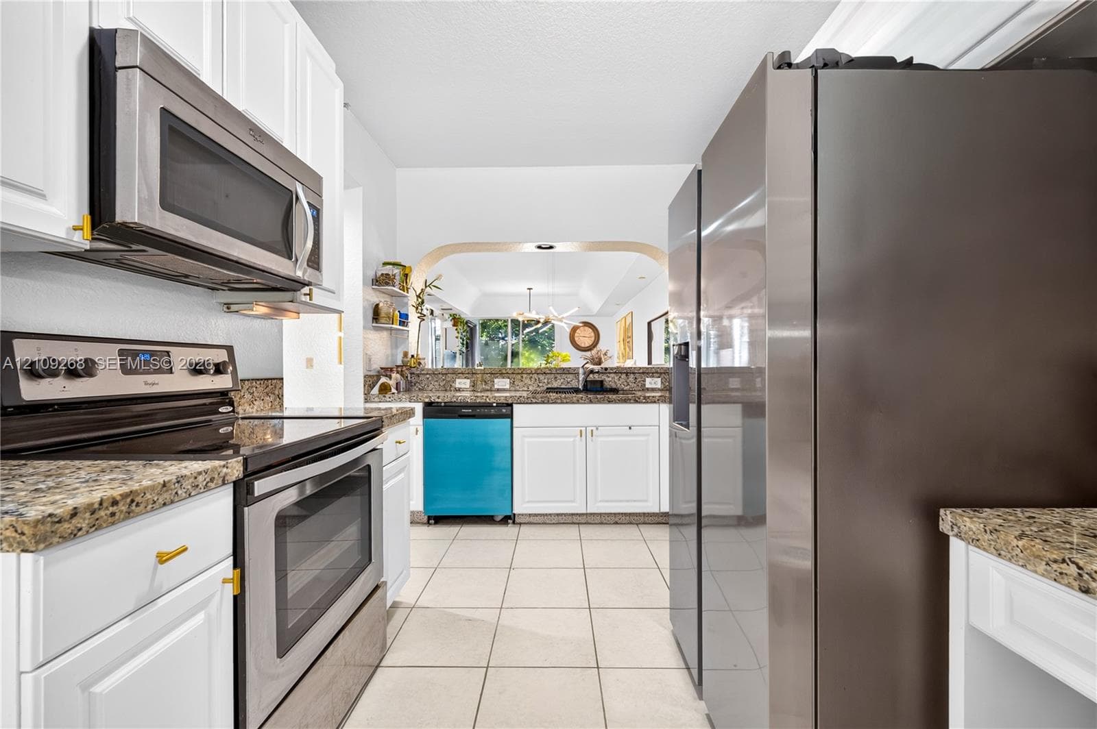 Kitchen featuring white cabinetry, stone-finish countertops, stainless steel appliances, ceramic tile flooring, and a pass-through window with an arched frame