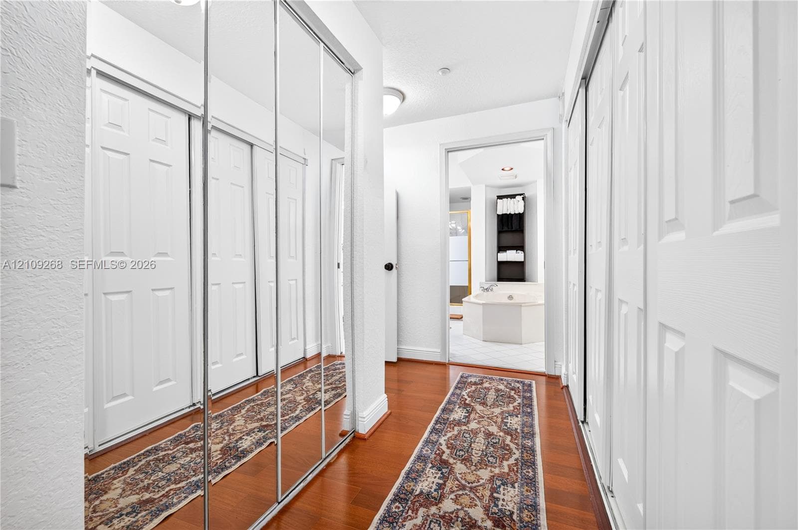 Hallway featuring wood-finish flooring, floor-to-ceiling mirrored sliding closet doors, and recessed lighting