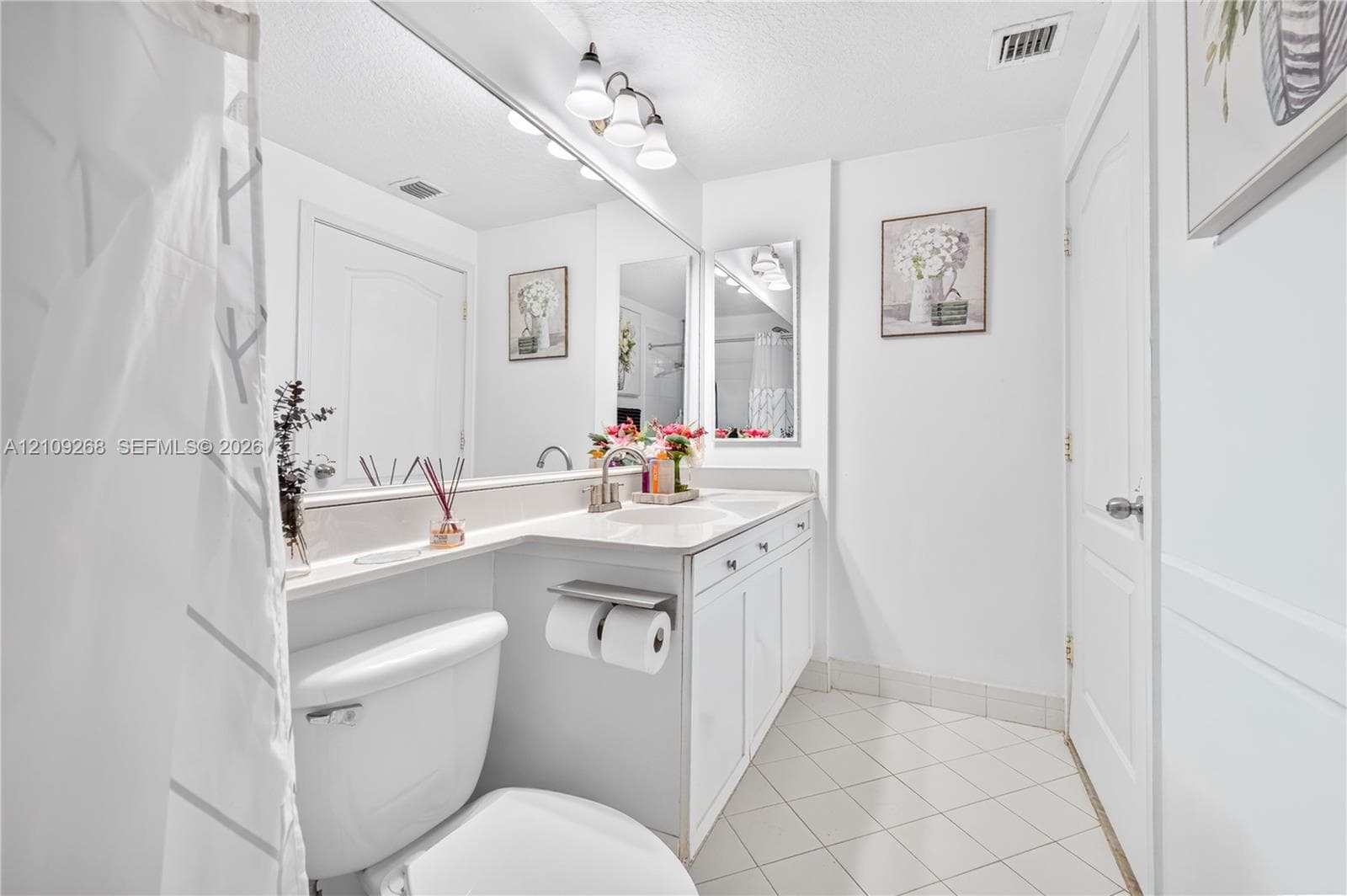 Bathroom featuring a white vanity cabinet with an integrated sink and countertop, full-width vanity mirror, polished metal fixtures, and diagonal tile flooring