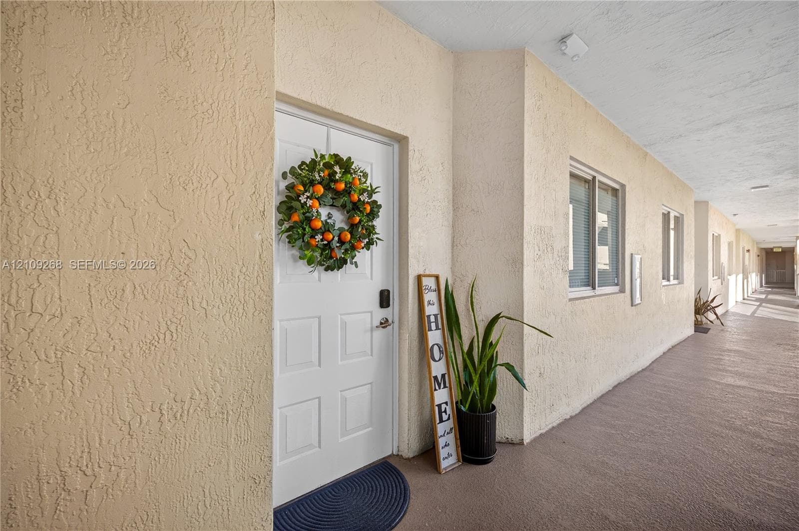Exterior entryway featuring textured stucco walls, a multi-panel door with electronic lock hardware, and an expansive covered walkway
