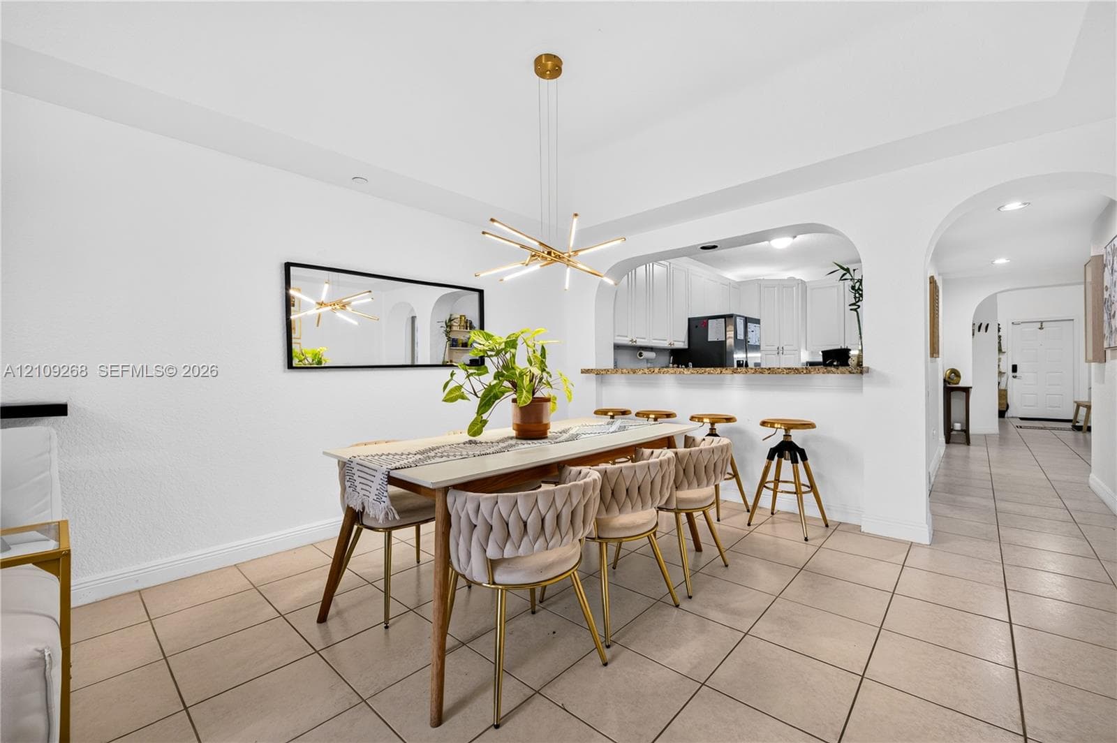 Dining area featuring tile flooring, a multi-light contemporary chandelier, arched architectural detailing, and a breakfast bar with stone-surface countertop