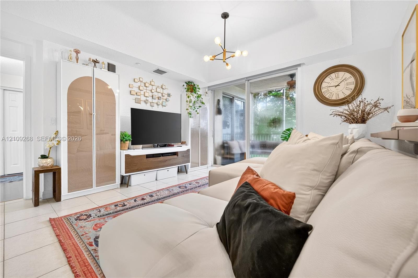 Tray ceiling, multi-light modern chandelier, large glass sliding doors, and light-toned tile flooring