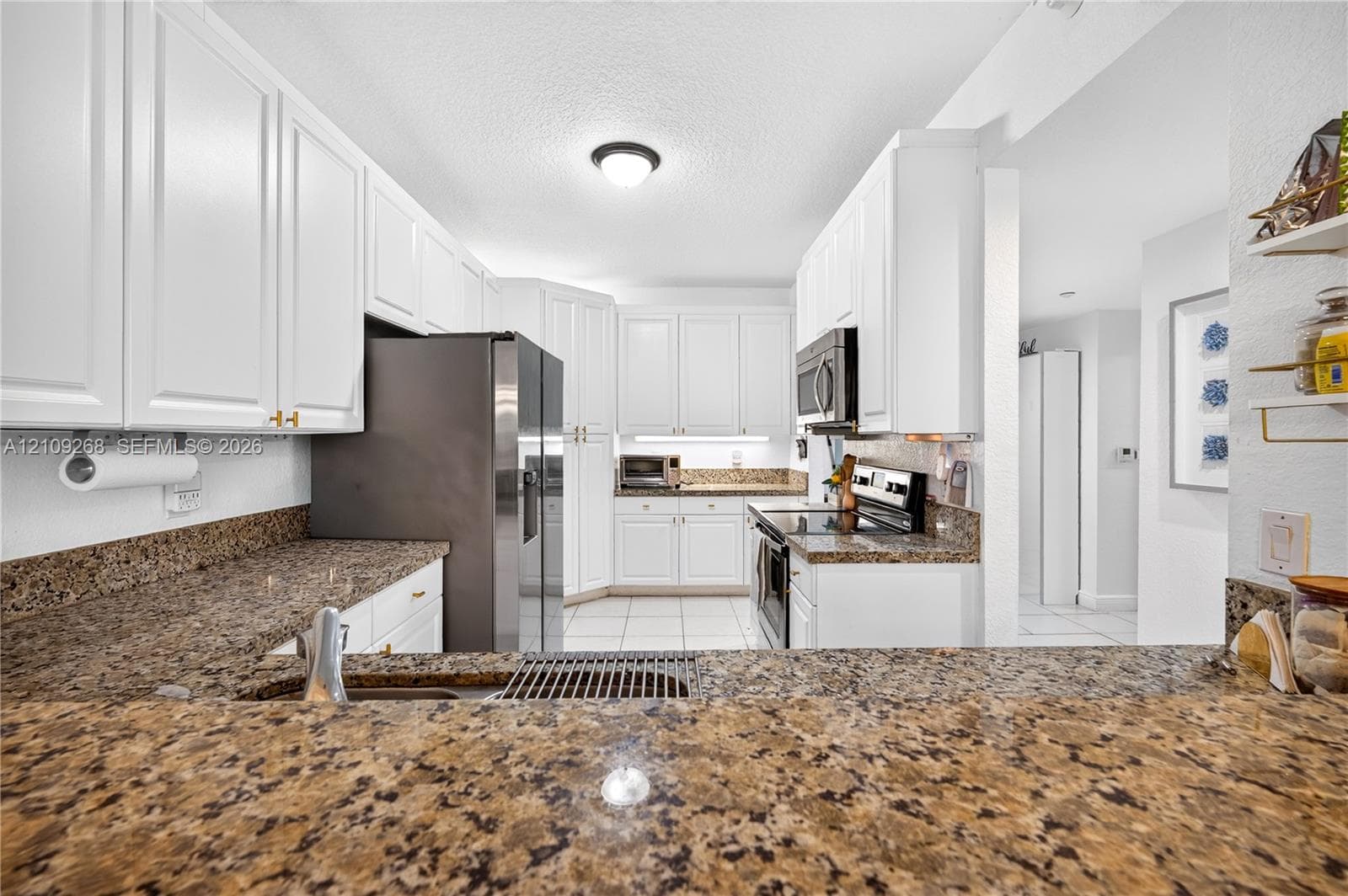 Kitchen featuring white cabinetry, stone-surface countertops, tile flooring, and stainless steel appliances