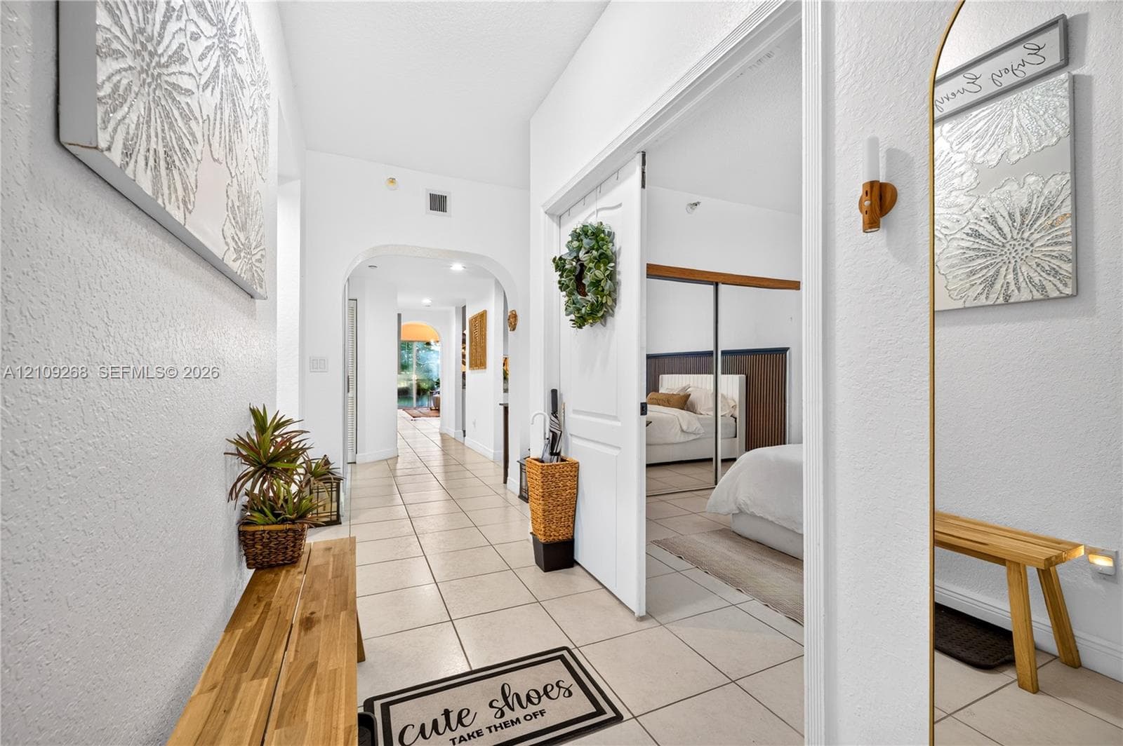 Interior hallway featuring neutral tile flooring, arched architectural details, and mirrored sliding closet doors