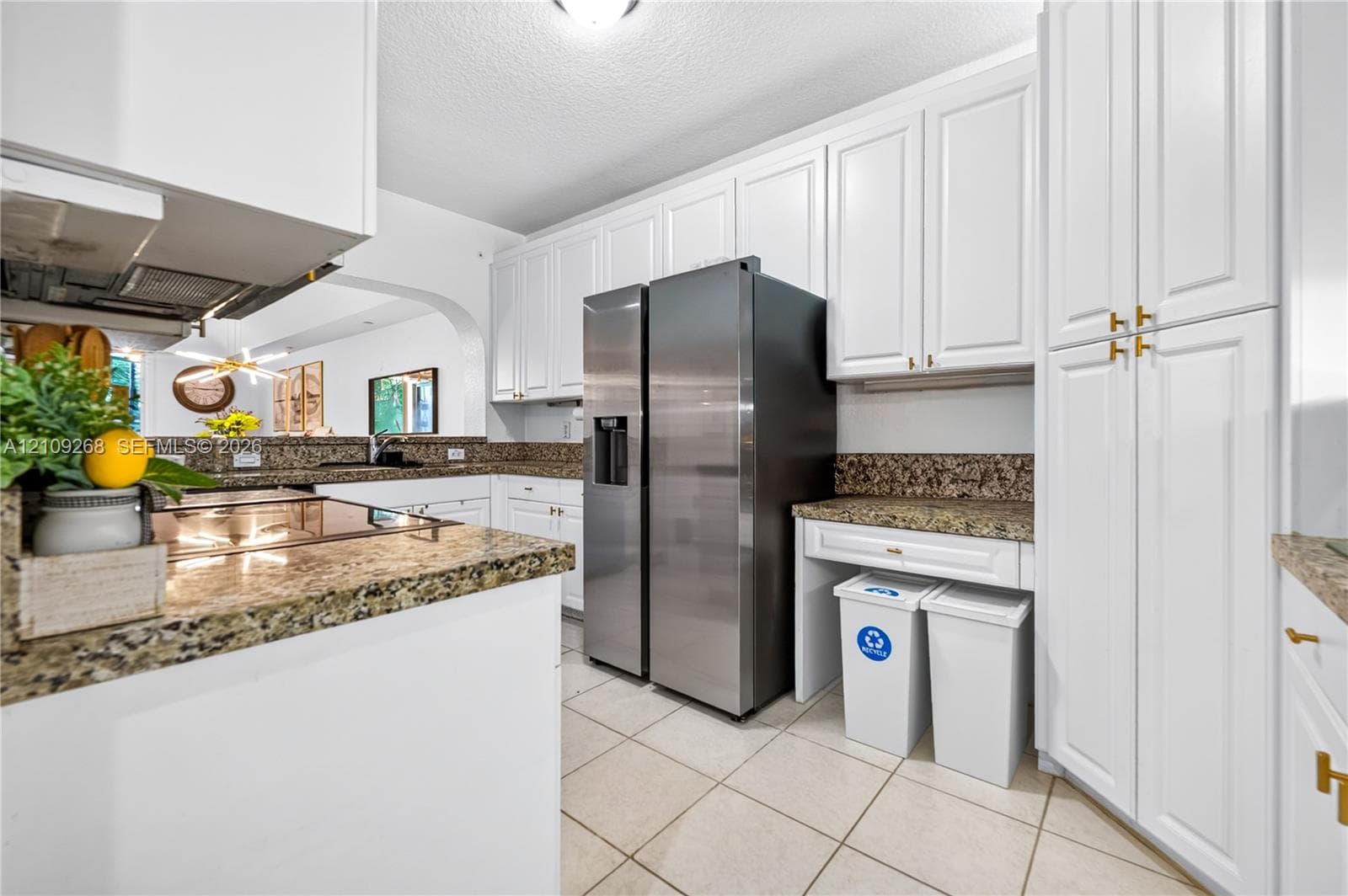 Kitchen featuring white shaker-style cabinetry, stone-finish countertops, stainless steel side-by-side refrigerator, tile flooring, and integrated built-in storage
