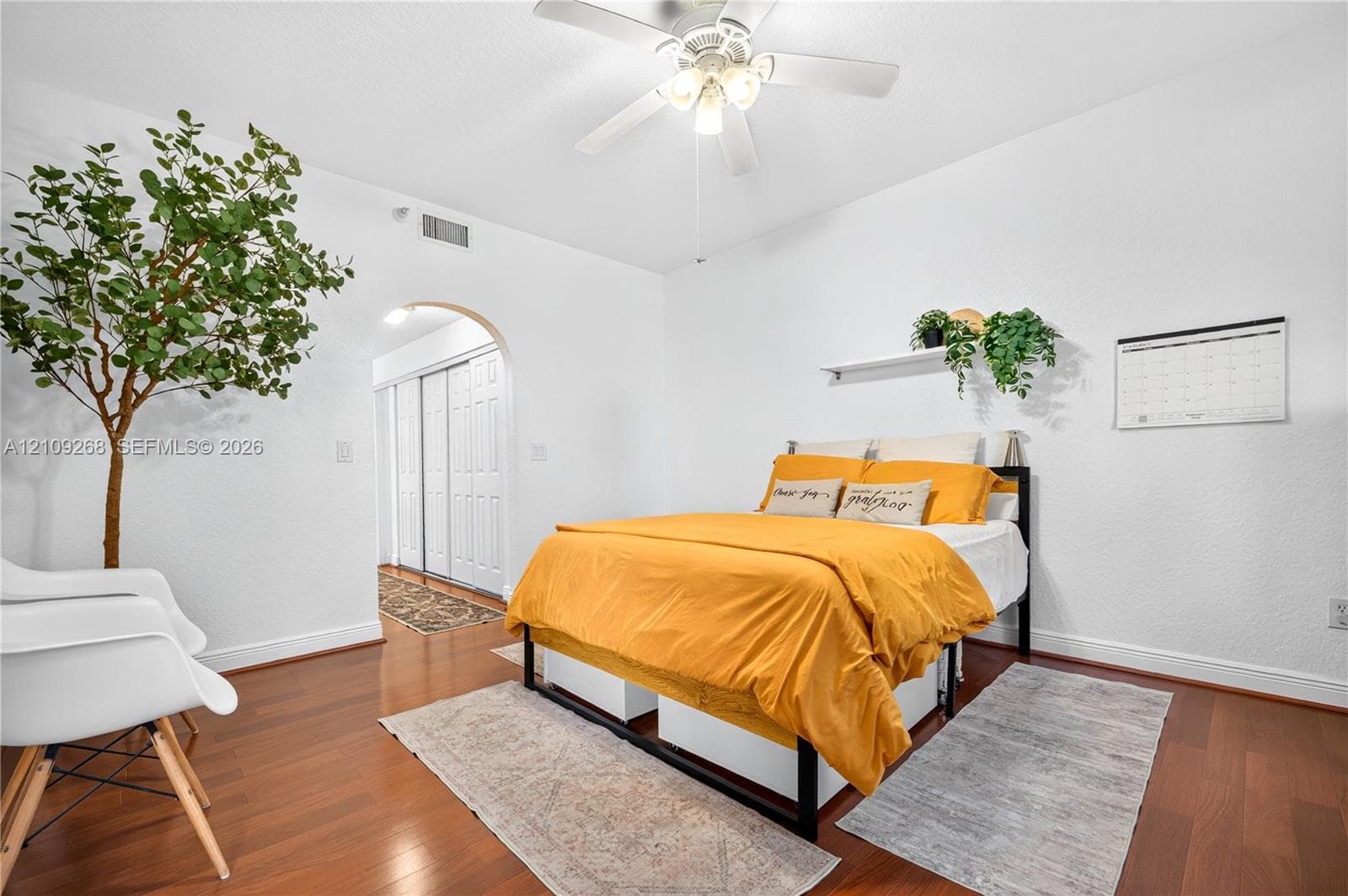 Room featuring wood-finish flooring, a ceiling fan with integrated lighting, an arched doorway, and built-in closet doors