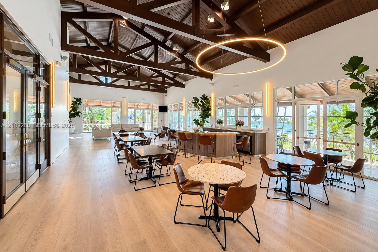 Open-concept interior featuring exposed wood-truss vaulted ceilings, wood-finish flooring, a built-in refreshment bar with quartz countertop, and expansive glass-paned doors