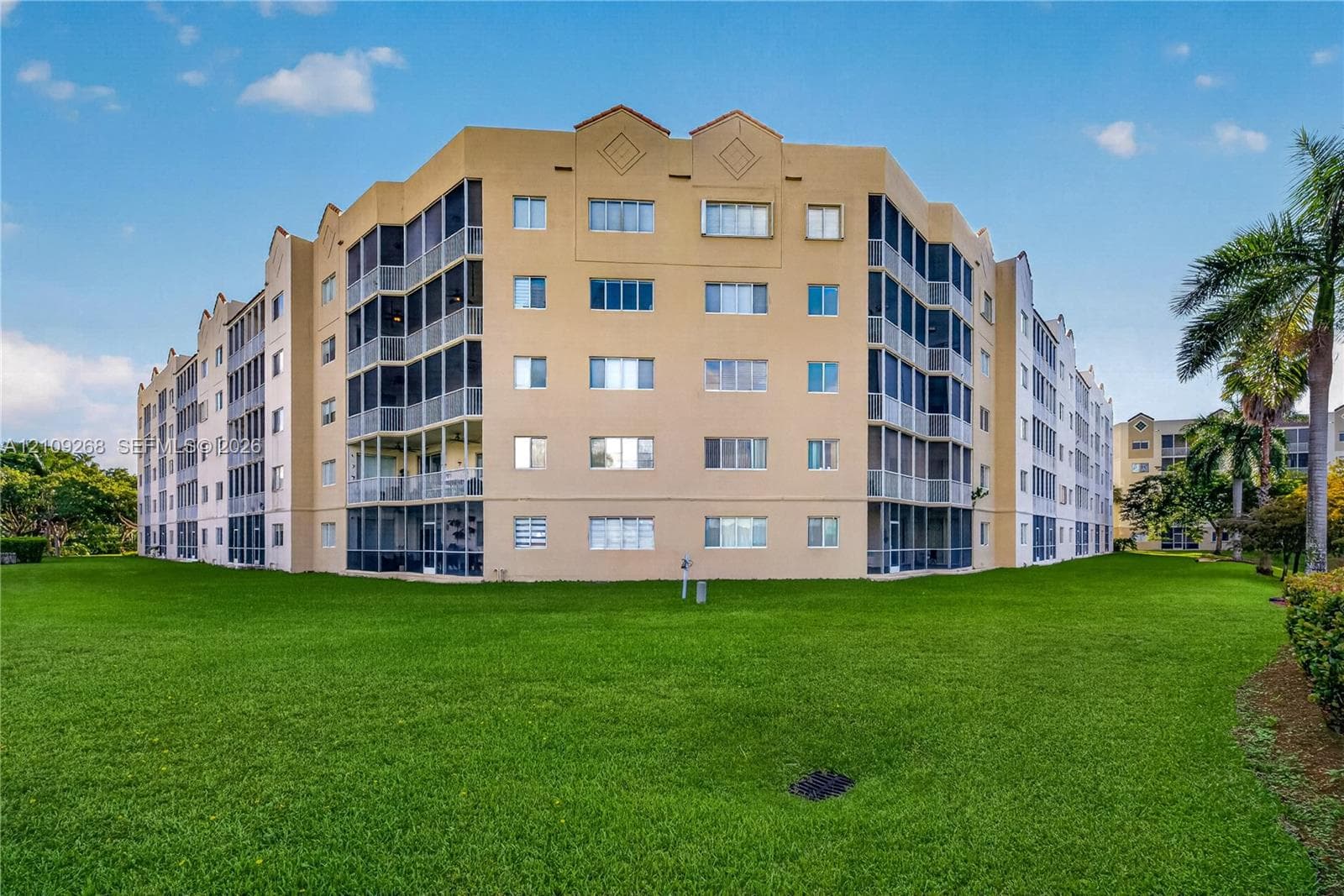 Multi-story residential building featuring a stucco exterior, integrated screened-in balconies, and expansive surrounding lawn areas