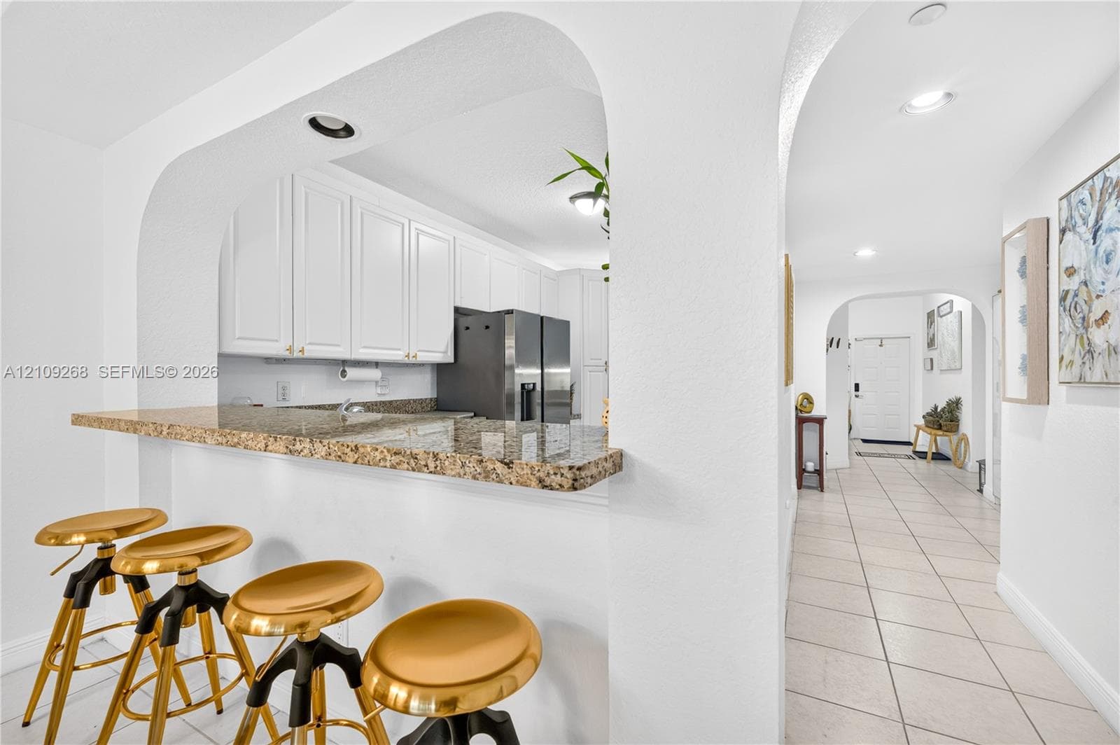 Kitchen featuring white cabinetry, stone-surface breakfast bar, recessed lighting, and arched architectural entryways with tile flooring