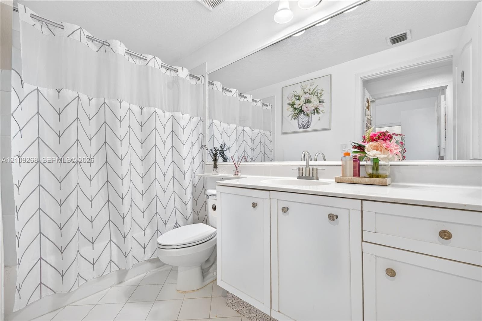 Bathroom featuring white cabinetry, an integrated basin, a large wall-mounted mirror, and tile flooring