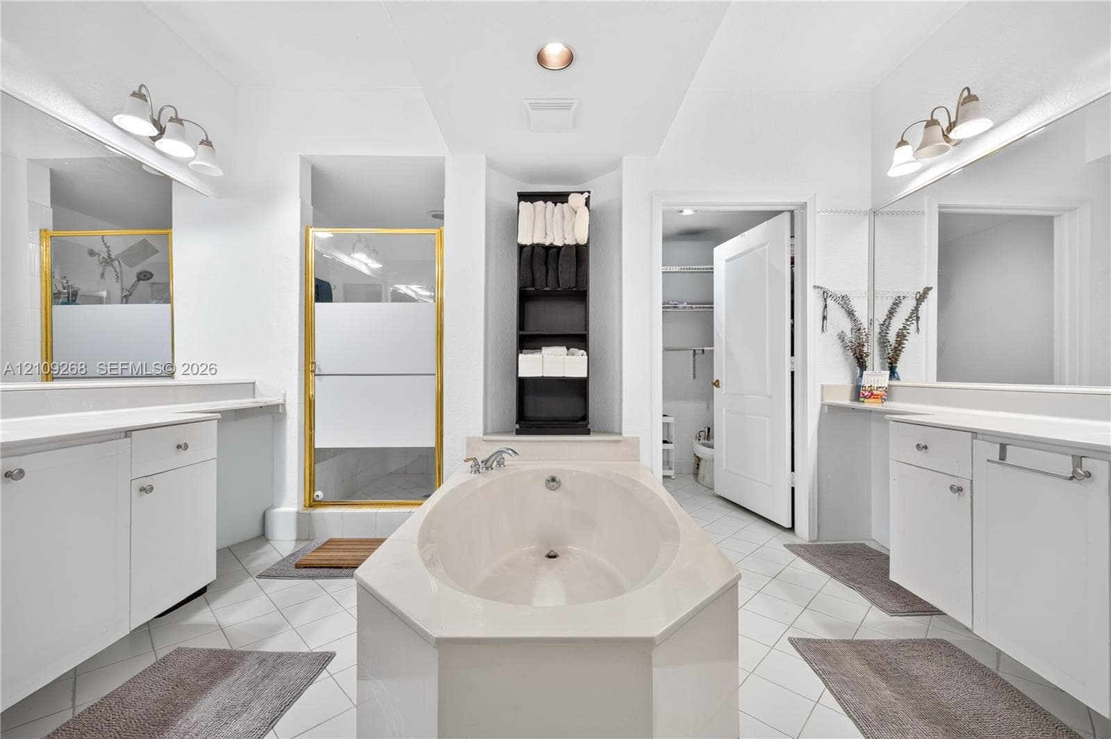 Bathroom featuring dual white vanities with solid-surface countertops, a center soaking tub, a glass-enclosed shower with metallic framing, and tile flooring