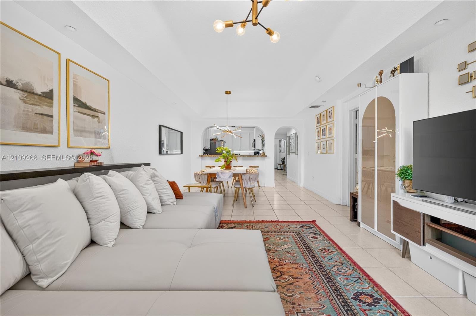 Tray ceiling, neutral tile flooring, modern multi-arm chandelier lighting, and arched architectural wall opening