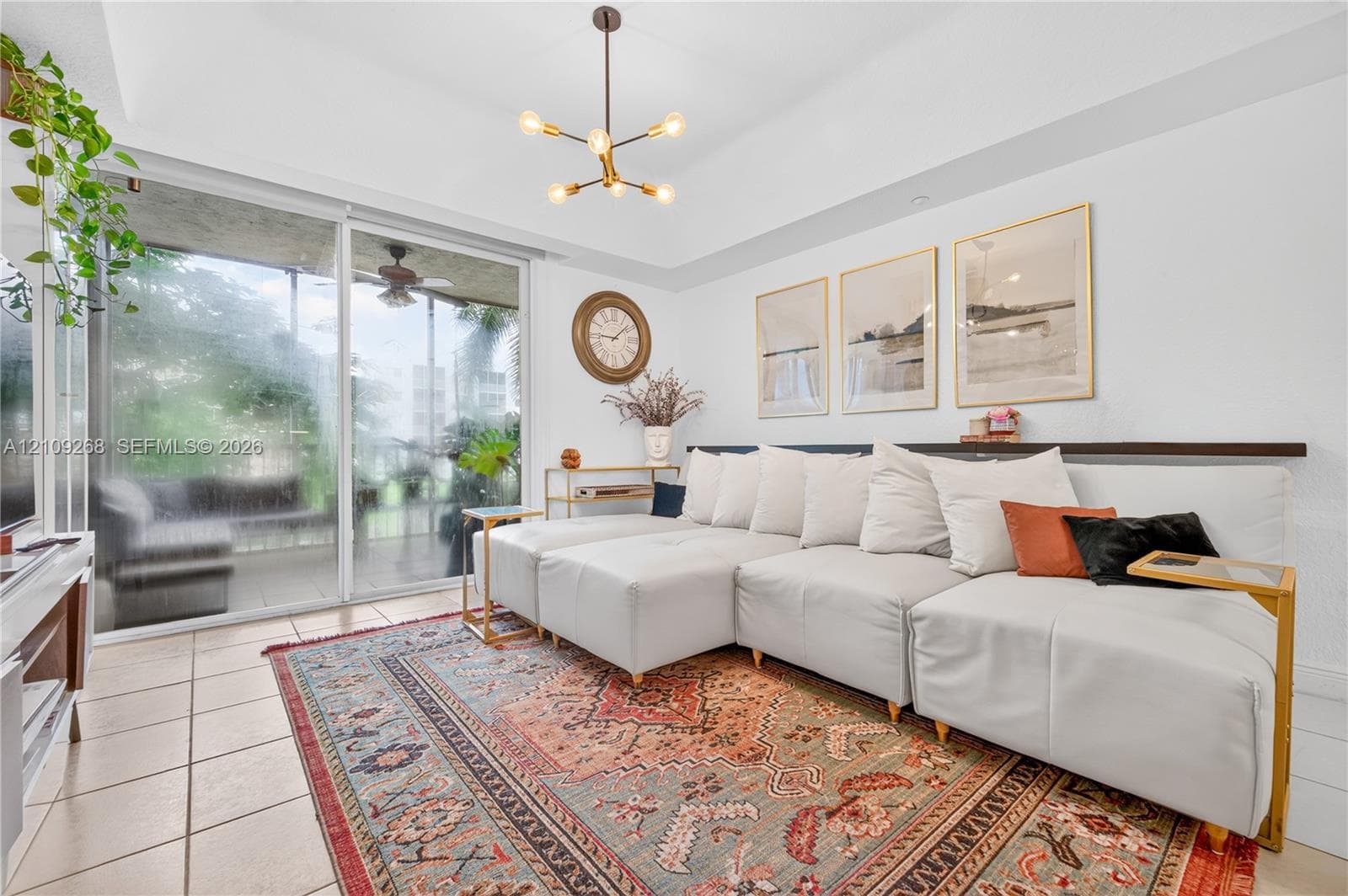 Living area featuring high ceilings, neutral tile flooring, a multi-arm modern light fixture, and floor-to-ceiling sliding glass doors opening to a covered balcony