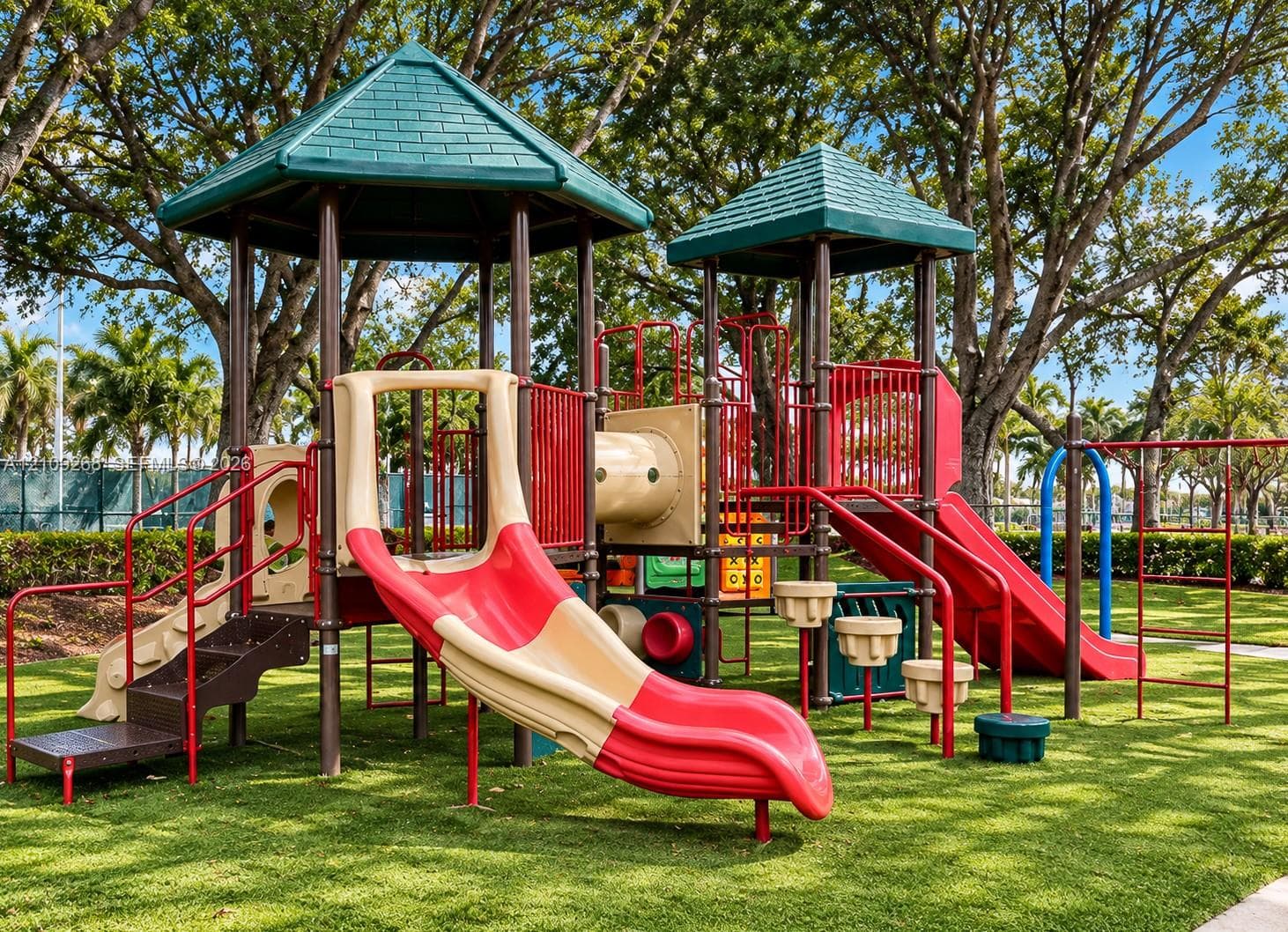 Outdoor playground structure featuring multi-level platforms, dual slide components, climbing stairs, and structural pillars on a manicured lawn