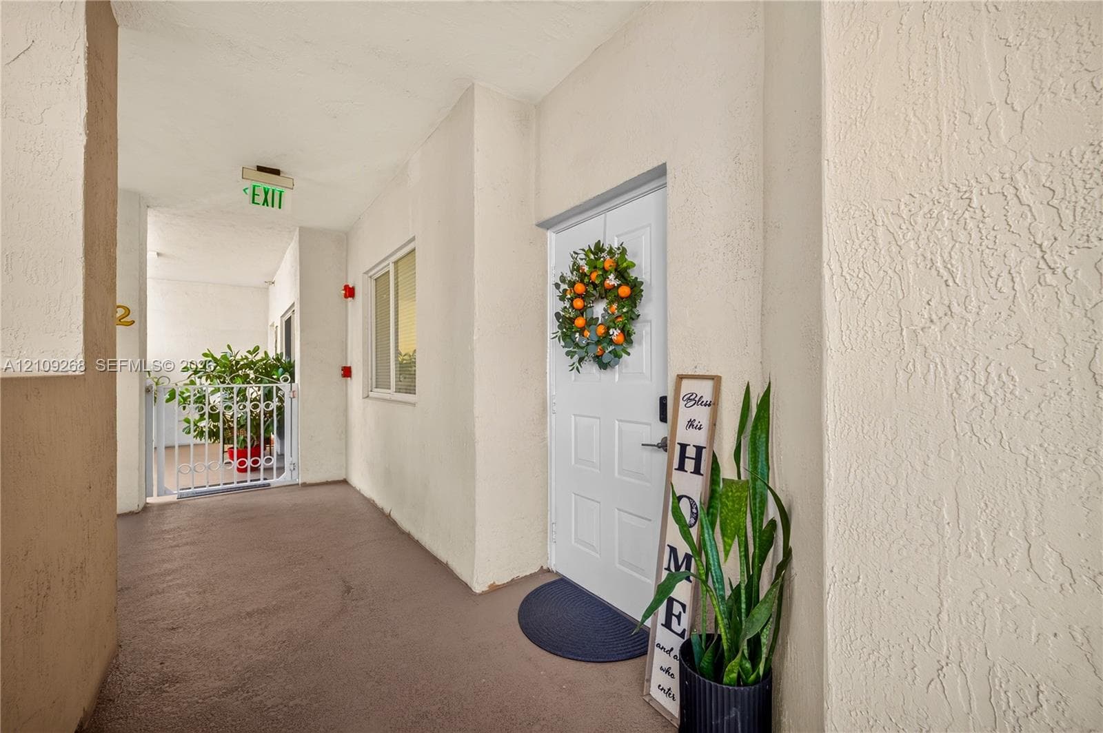 Covered exterior entryway featuring textured wall finishes, a solid core white paneled door, and metal railing enclosure