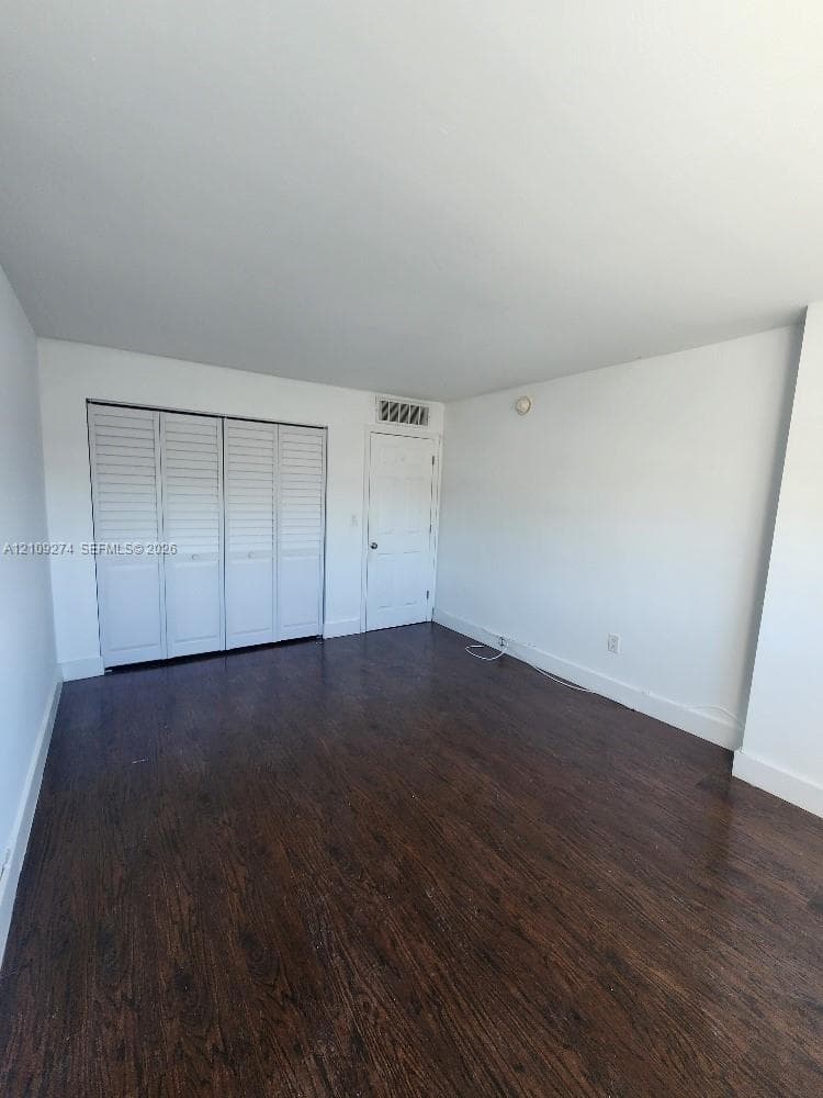 Interior space featuring wood-finish flooring, white walls, louvered bi-fold closet doors, and a solid-core interior door