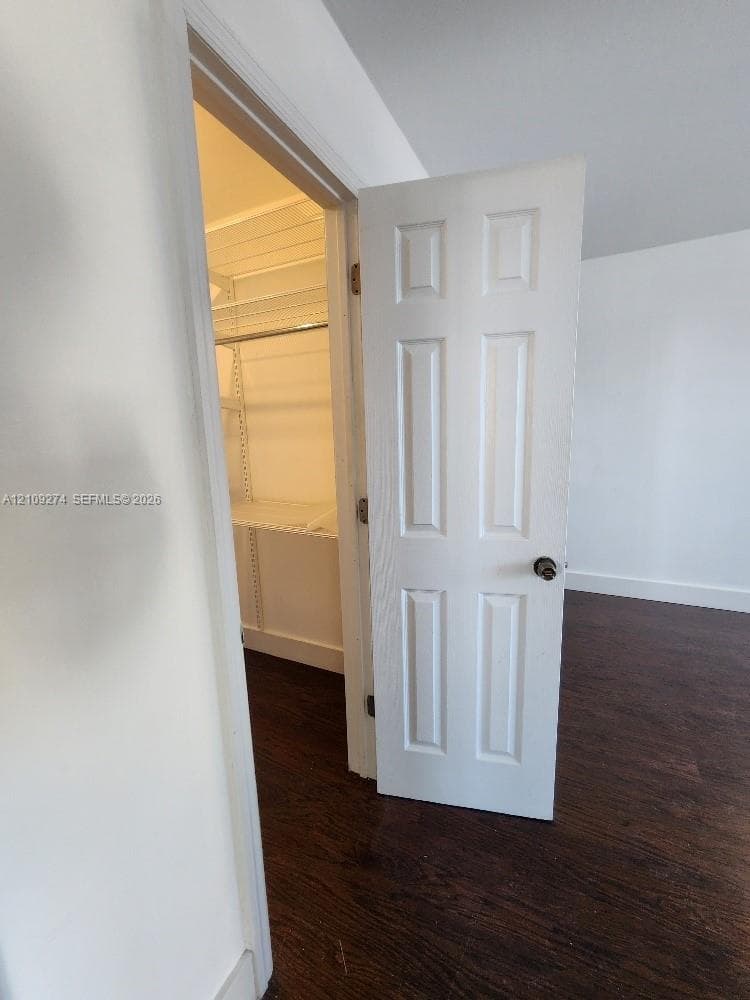 Six-panel interior door with a round knob, dark wood-finish flooring, and built-in wire shelving