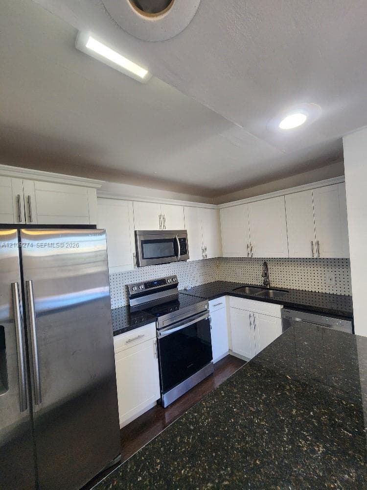 Kitchen featuring white shaker-style cabinetry, dark stone countertops, stainless steel appliances, a tiled backsplash, and recessed lighting