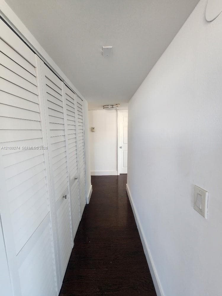 Hallway featuring dark wood-finish flooring, white walls, and built-in closet storage with louvered doors