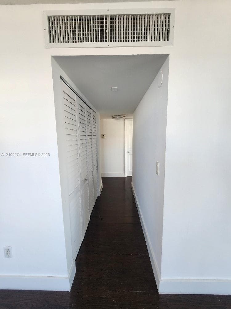Hallway featuring dark wood-finish flooring, white louvered closet doors, and a ceiling-mounted light fixture