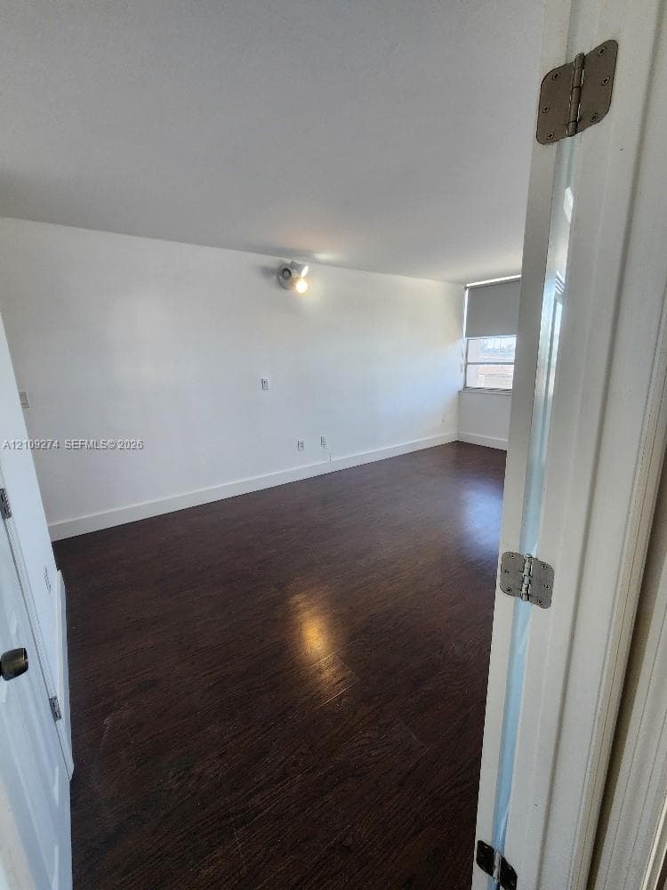 Interior space featuring dark wood-finish flooring, neutral wall tones, wall-mounted lighting, and a roller shade