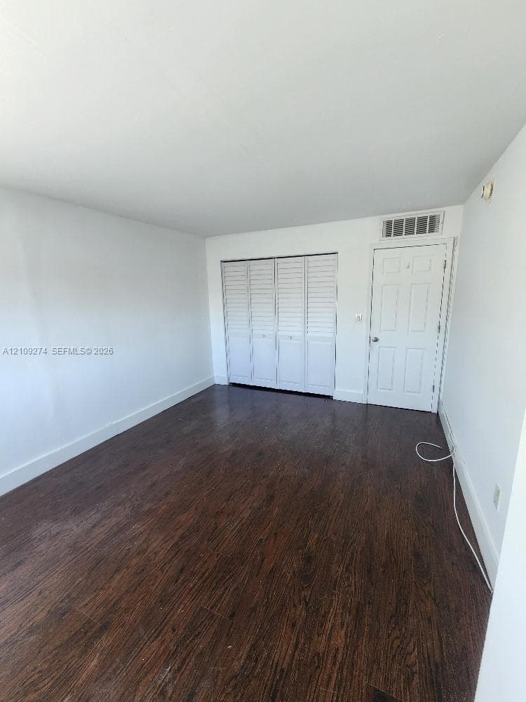 Room featuring wood-finish flooring, white walls, and a four-panel louvered closet door