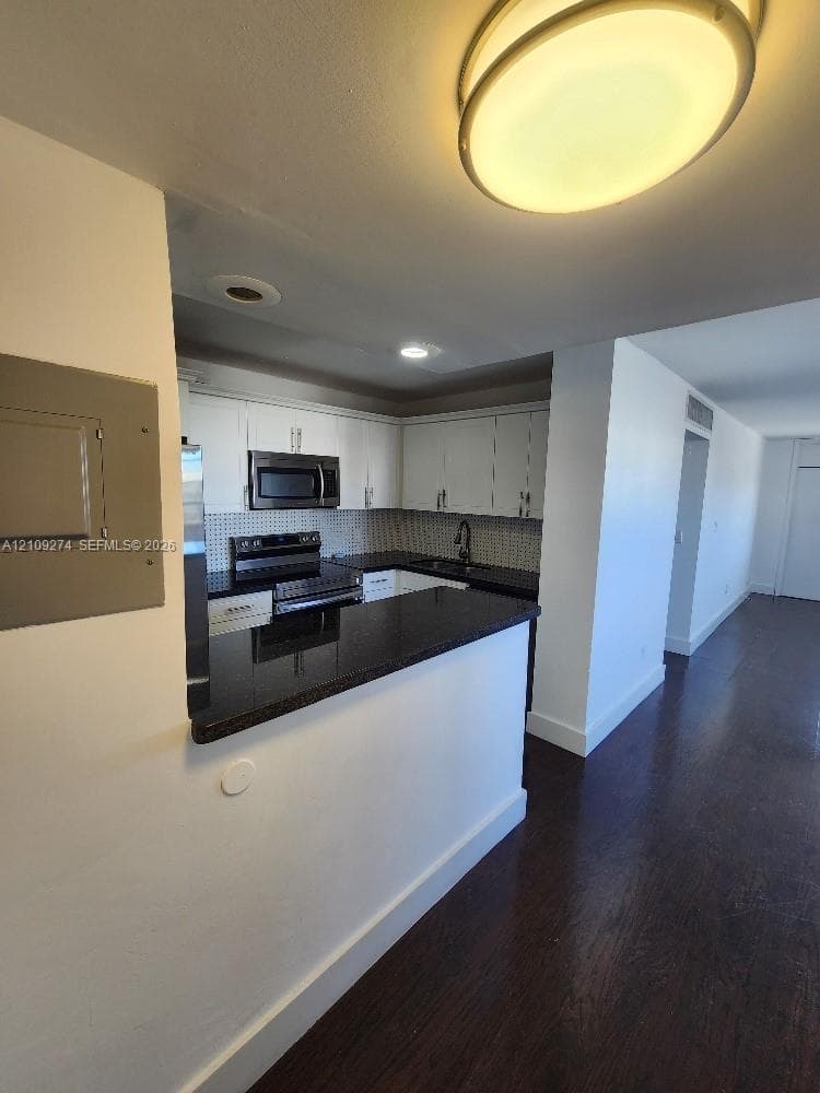 Kitchen featuring white cabinetry, dark countertops, a built-in microwave, a dark-finish faucet, and wood-finish flooring