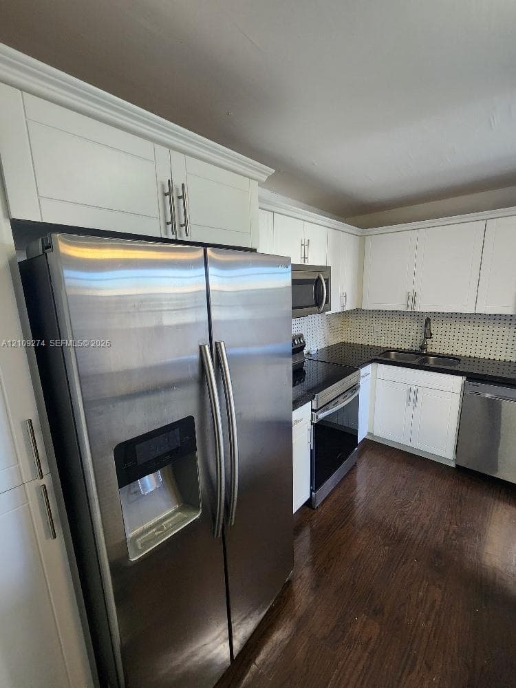 Kitchen featuring white shaker-style cabinetry, stainless steel appliances, dark stone-finish countertops, mosaic tile backsplash, and dark wood-finish flooring