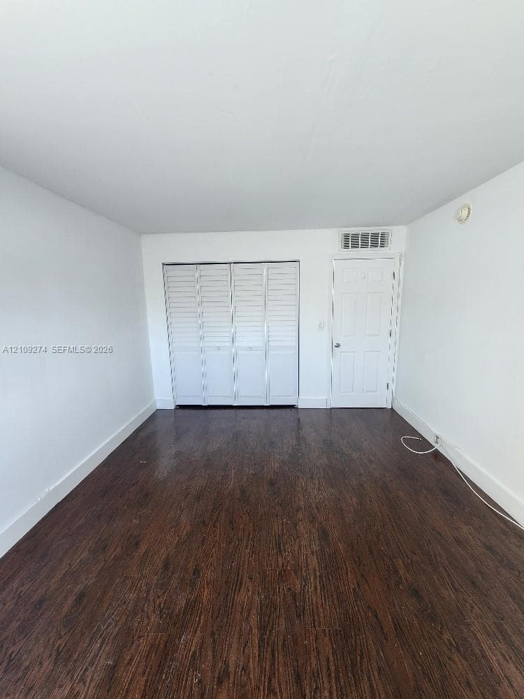 Interior room featuring dark wood-finish flooring, white walls, and a multi-panel louvered closet door