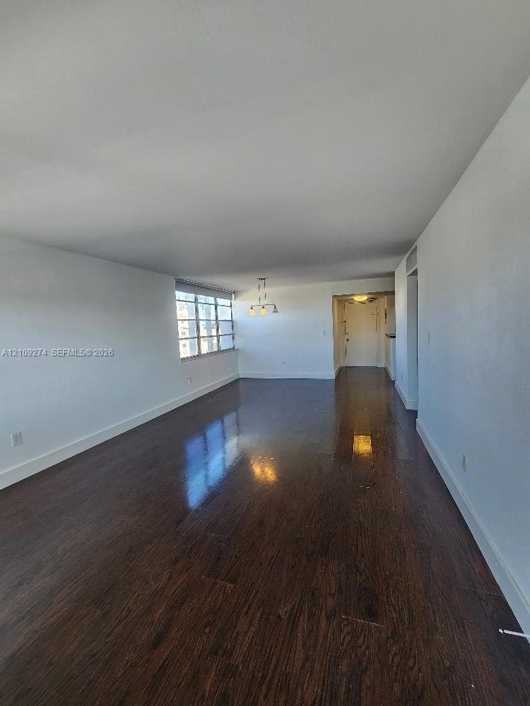 Expansive room featuring dark wood-finish flooring, white walls, large multi-pane window, and decorative pendant lighting