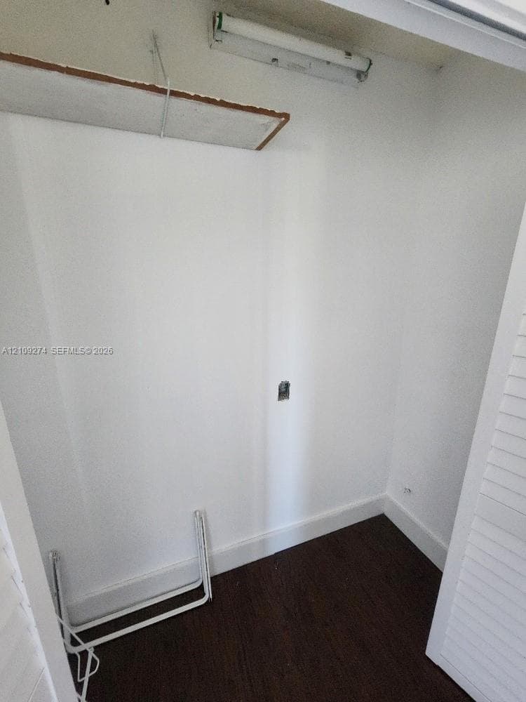 Closet featuring wood-finish flooring, white walls, built-in shelving, and overhead lighting
