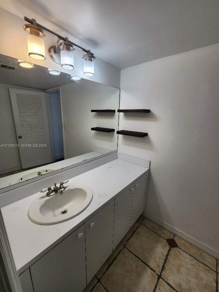Vanity featuring a white countertop, inset sink, chrome faucet, wall-mounted light fixture, large mirror, and built-in floating wall shelves