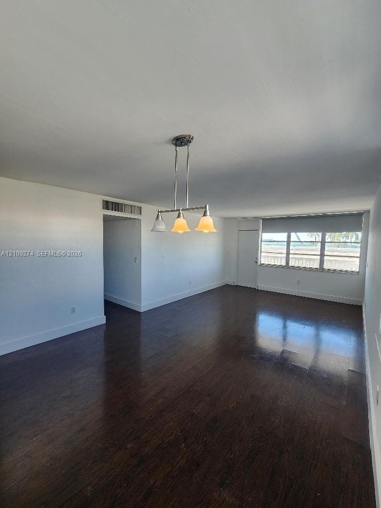 Open-concept interior featuring dark wood-finish flooring, a multi-light brushed-metal chandelier, and expansive windows with exterior water scenery