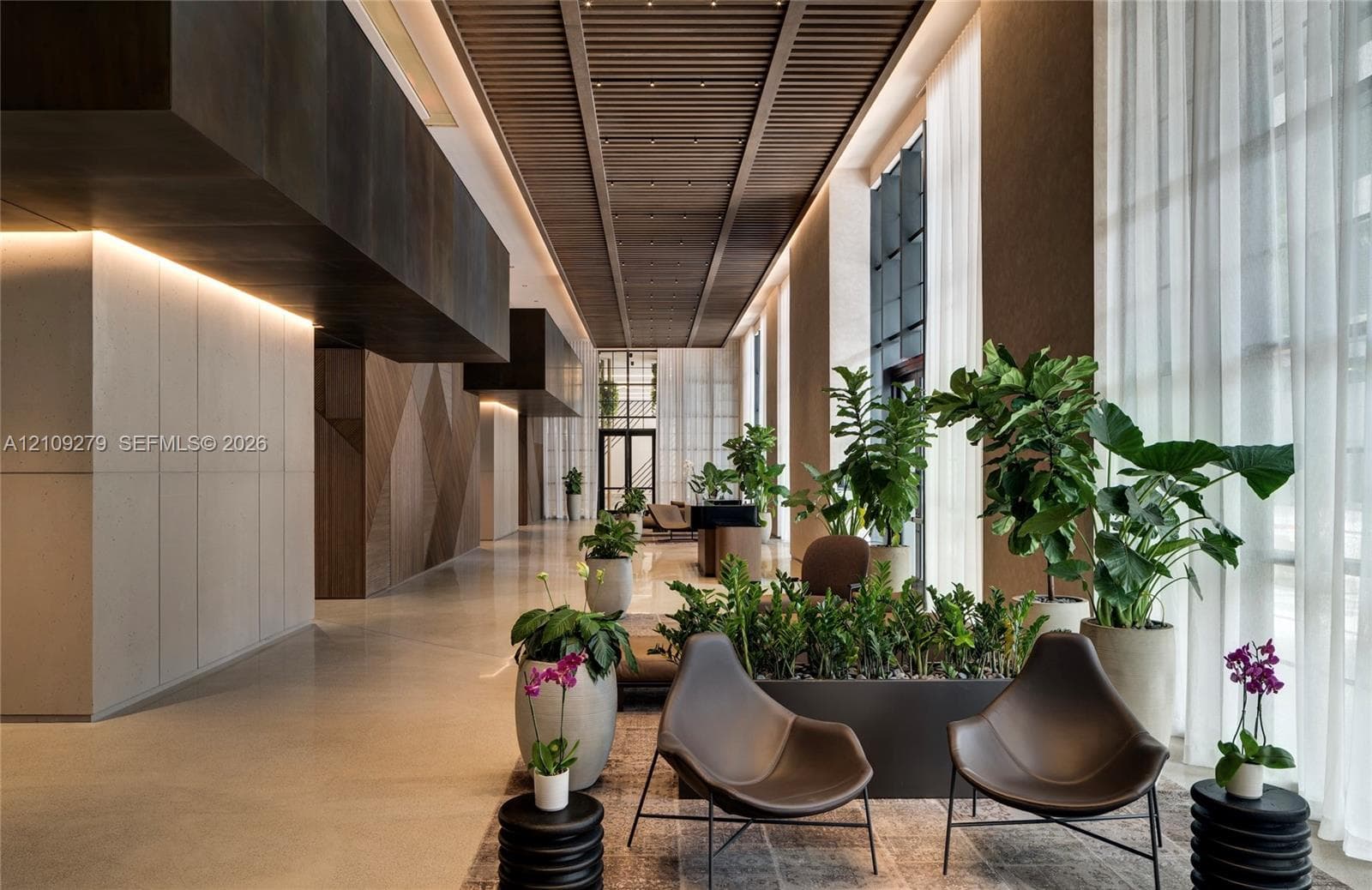 Expansive lobby featuring a linear wood-slat ceiling, recessed cove lighting, floor-to-ceiling drapery, and a polished concrete floor