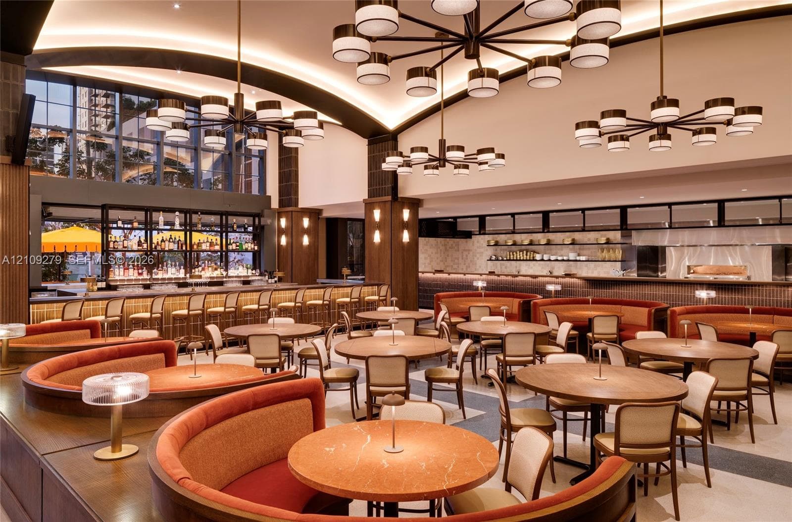 Spacious dining area featuring vaulted ceilings with recessed accent lighting, multiple large-scale multi-arm chandeliers, integrated curved banquet seating, and a full-length service bar with overhead shelving