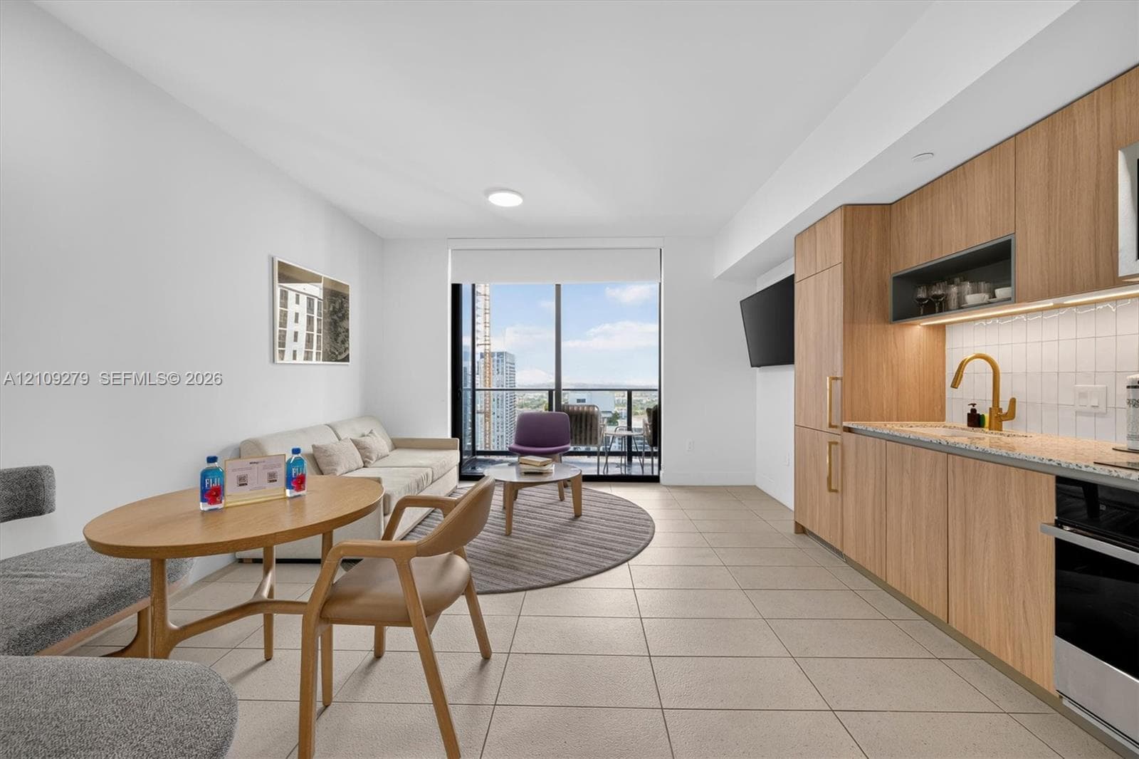 Modern kitchen featuring flat-panel wood-finish cabinetry, stone countertops, square-tile backsplash, and a gold-tone gooseneck faucet, highlighted by floor-to-ceiling windows and large-format tile flooring