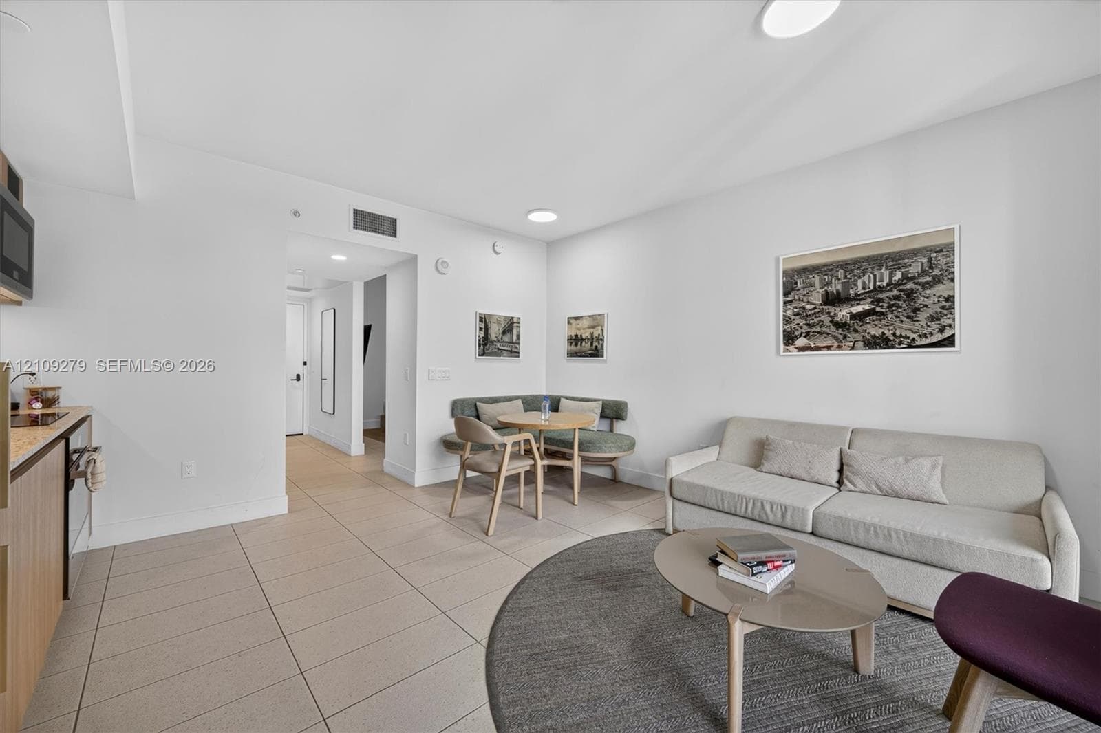 Open-concept interior featuring light-toned tile flooring, recessed ceiling lighting, and a kitchen area with wood-finish cabinetry