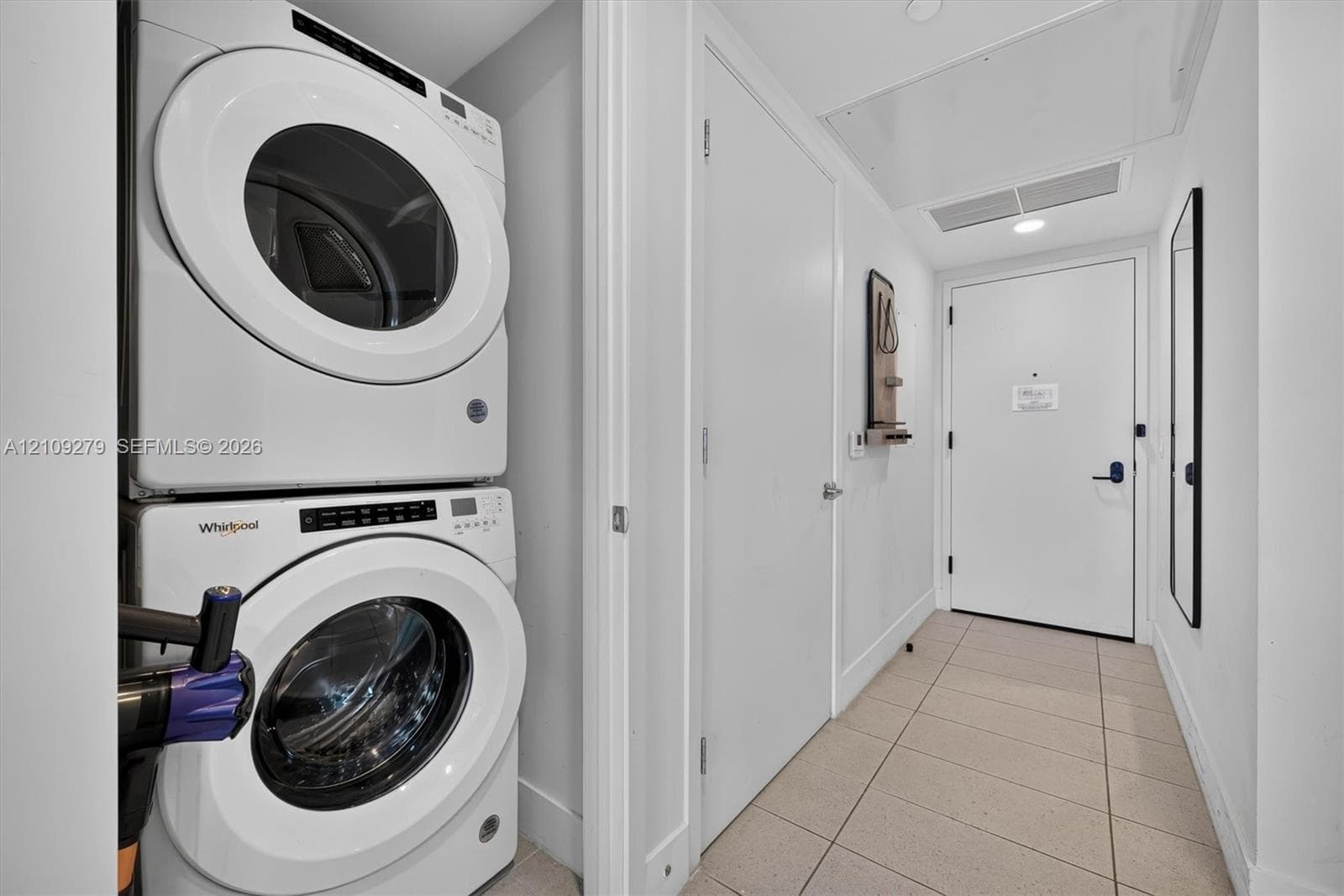 Stacked laundry unit featuring white front-loading appliances, neutral tile flooring, and solid-core interior doors