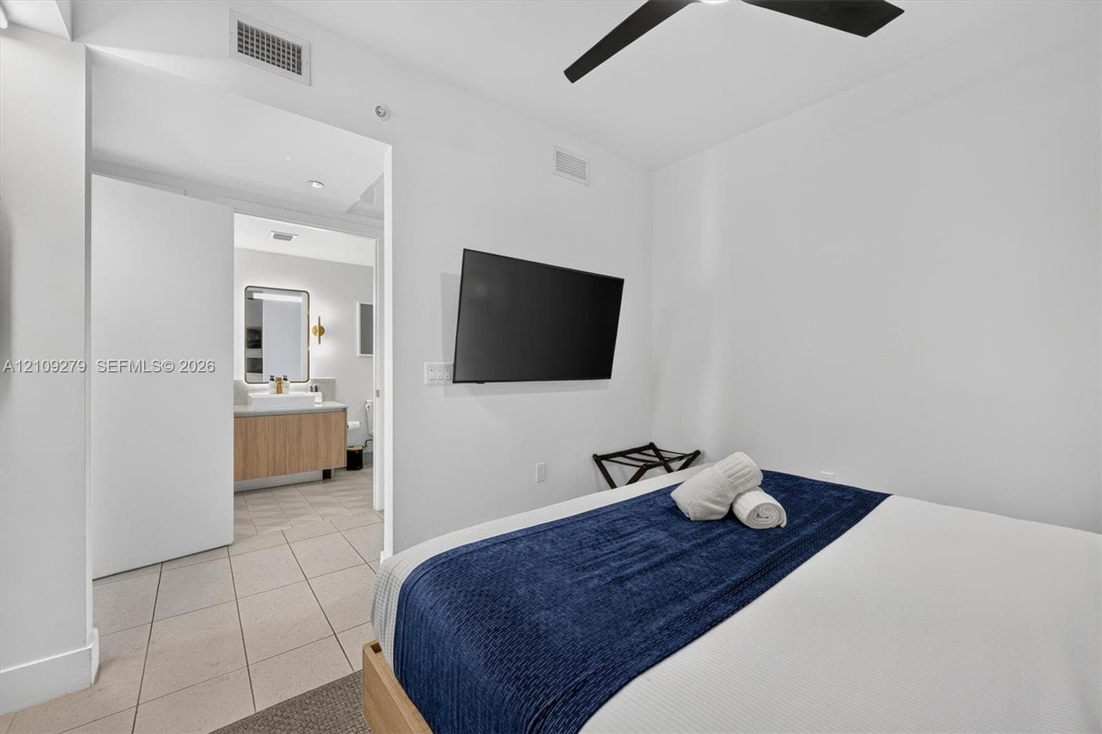 Neutral-toned tile flooring, matte black ceiling fan with integrated lighting, and white walls