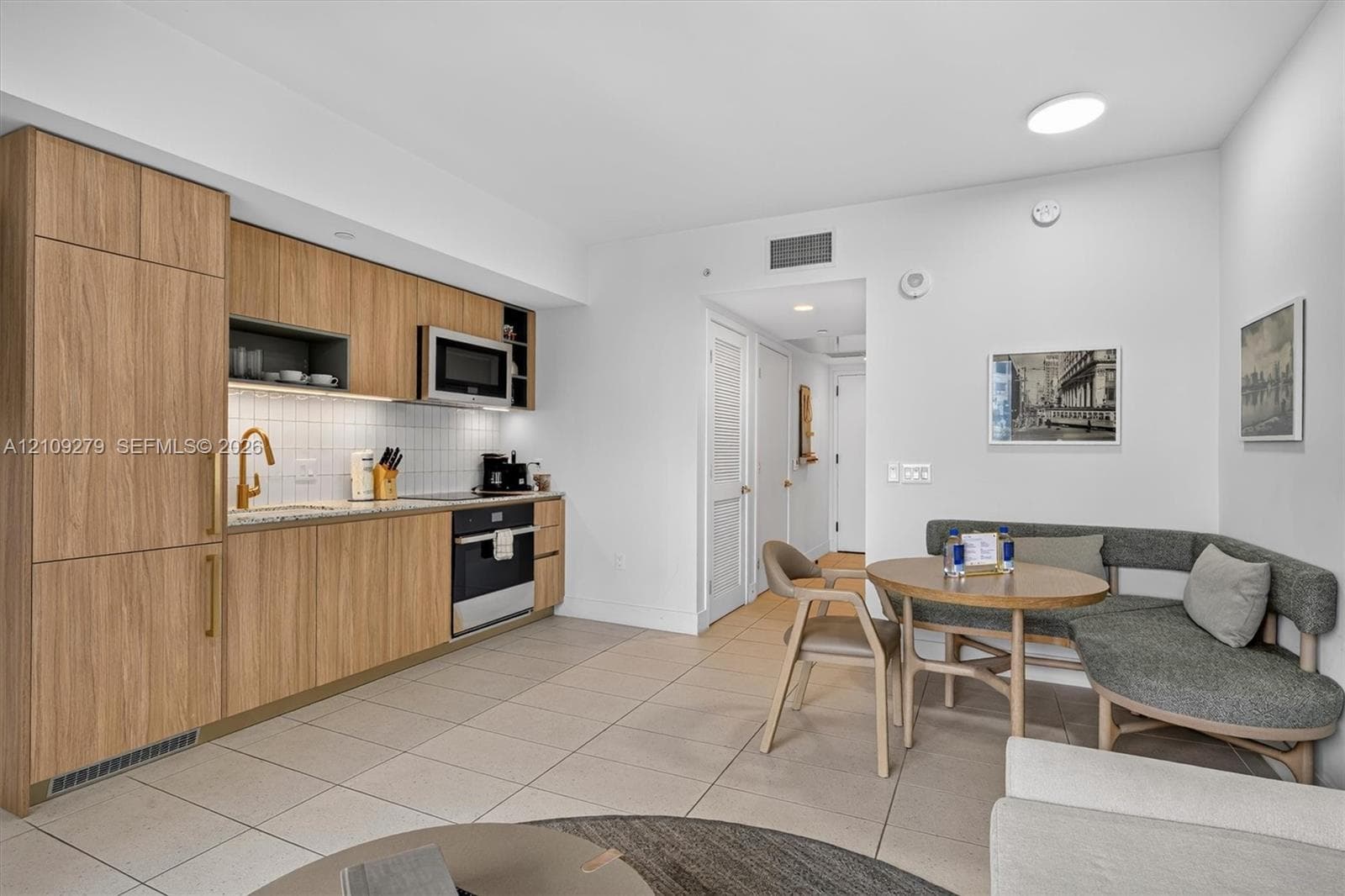 Kitchen featuring light wood-finish cabinetry, integrated refrigerator, stone-style countertop, white tile backsplash, and stainless steel built-in oven