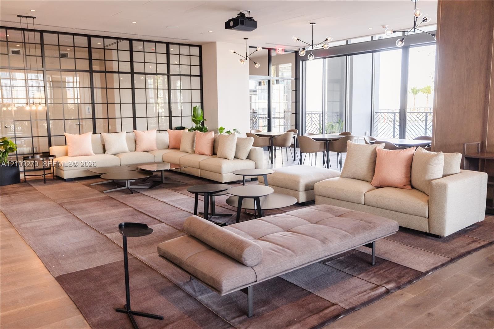 Open-concept common area featuring floor-to-ceiling metal-framed grid glass partitions, wood-finish flooring, expansive floor-to-ceiling windows, and modern multi-arm light fixtures