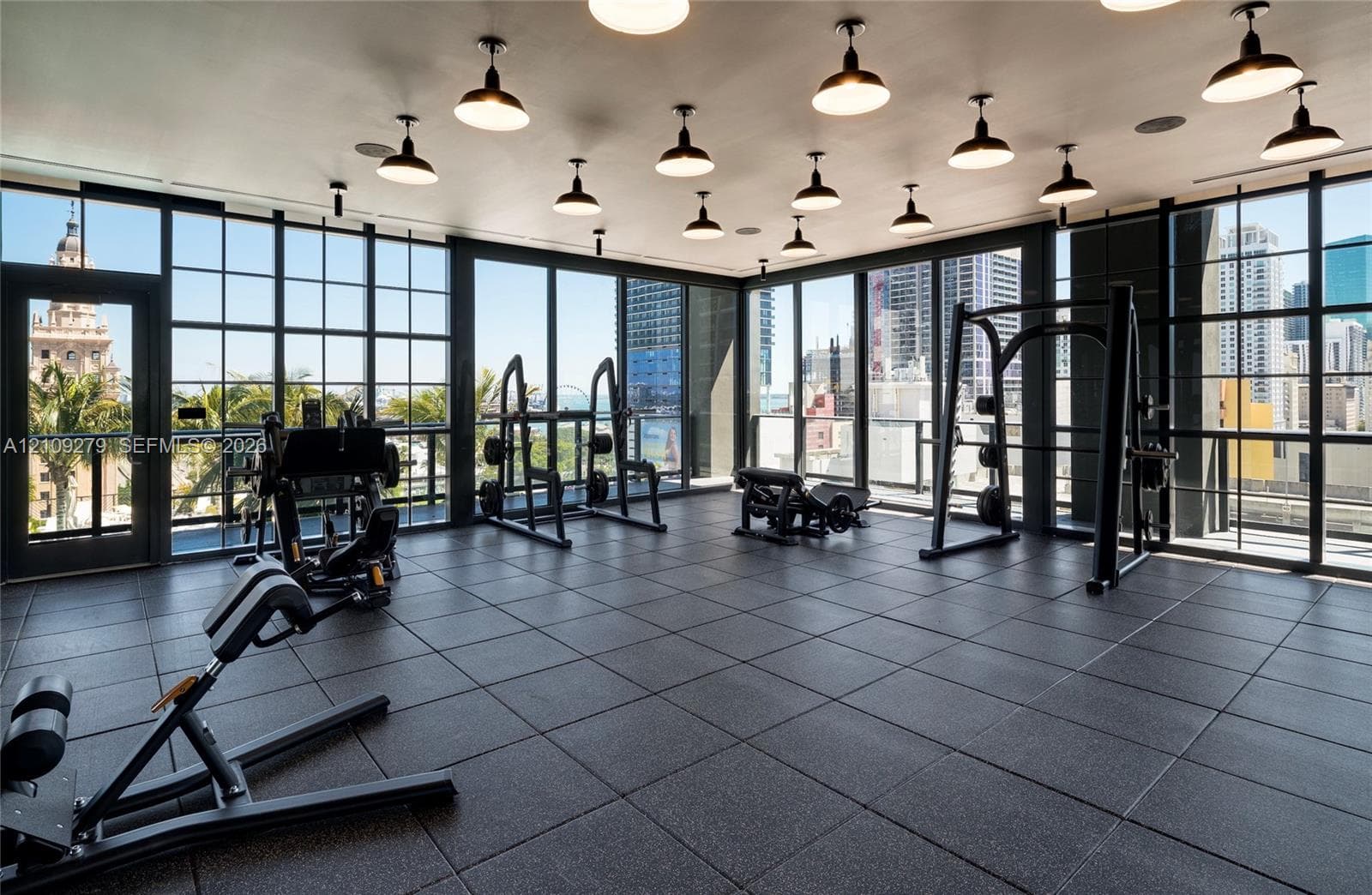 Fitness space featuring floor-to-ceiling industrial-style steel frame windows, rubberized modular flooring, and recessed pendant lighting
