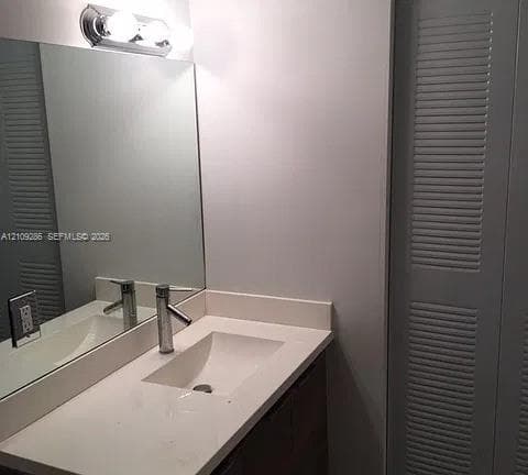 Vanity featuring a solid-surface countertop, rectangular integrated basin, single-handle metal faucet, large wall-mounted mirror, and louvered-style cabinet doors