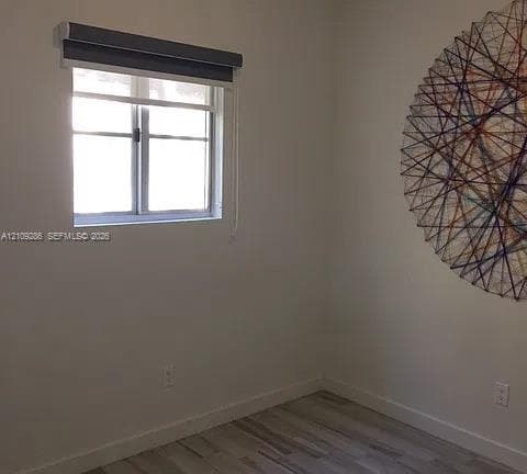 Neutral-toned interior space featuring wood-finish flooring and a single-hung window with a charcoal-toned roller shade